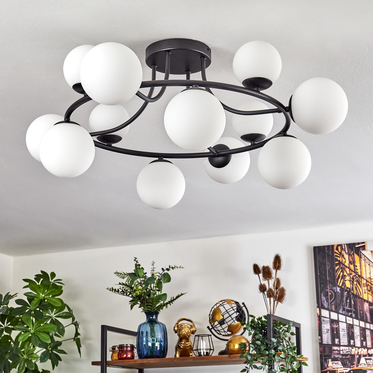 Eine moderne Deckenleuchte mit weißen Kugellampen. Darunter ein Regal mit Dekoration: Vase, goldener Hund, Globus und Kunst.