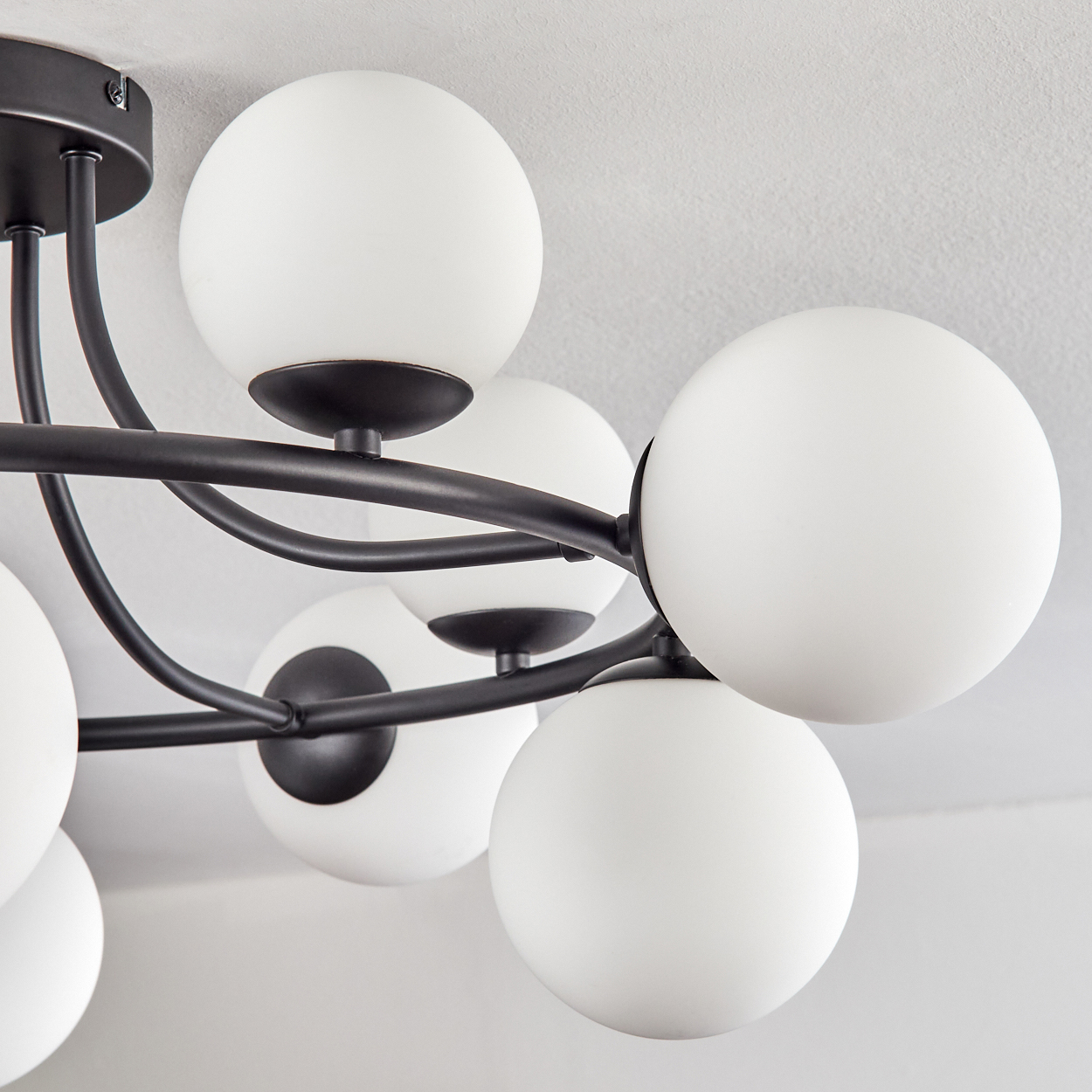 Eine moderne schwarze Pendelleuchte mit mehreren weißen Kugelleuchten an einer weißen Decke.