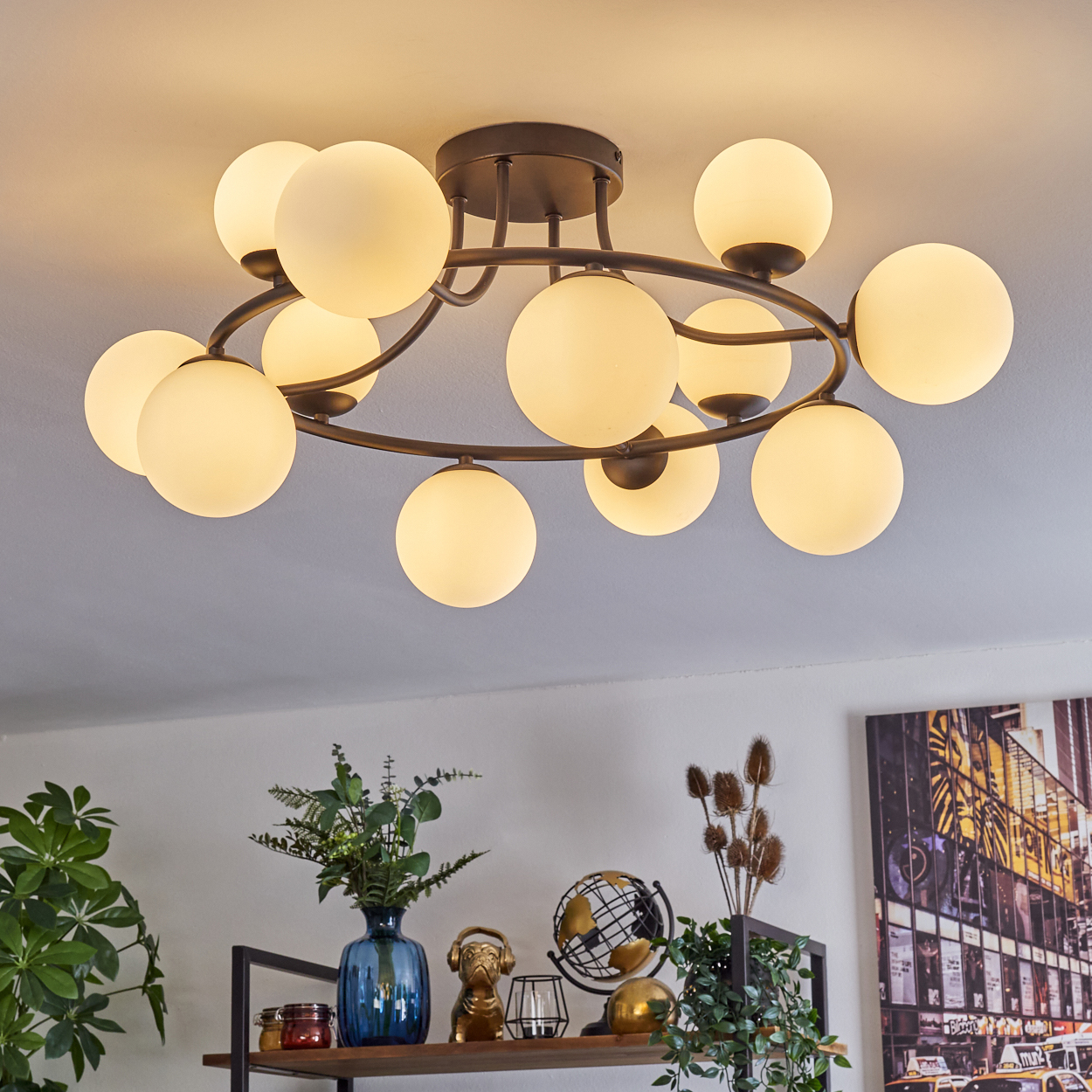 Moderne Deckenleuchte mit vielen kugelförmigen Glühbirnen. Darunter ein Regal mit Vase, Globus und Kunstdruck. Die Decke ist weiß.
