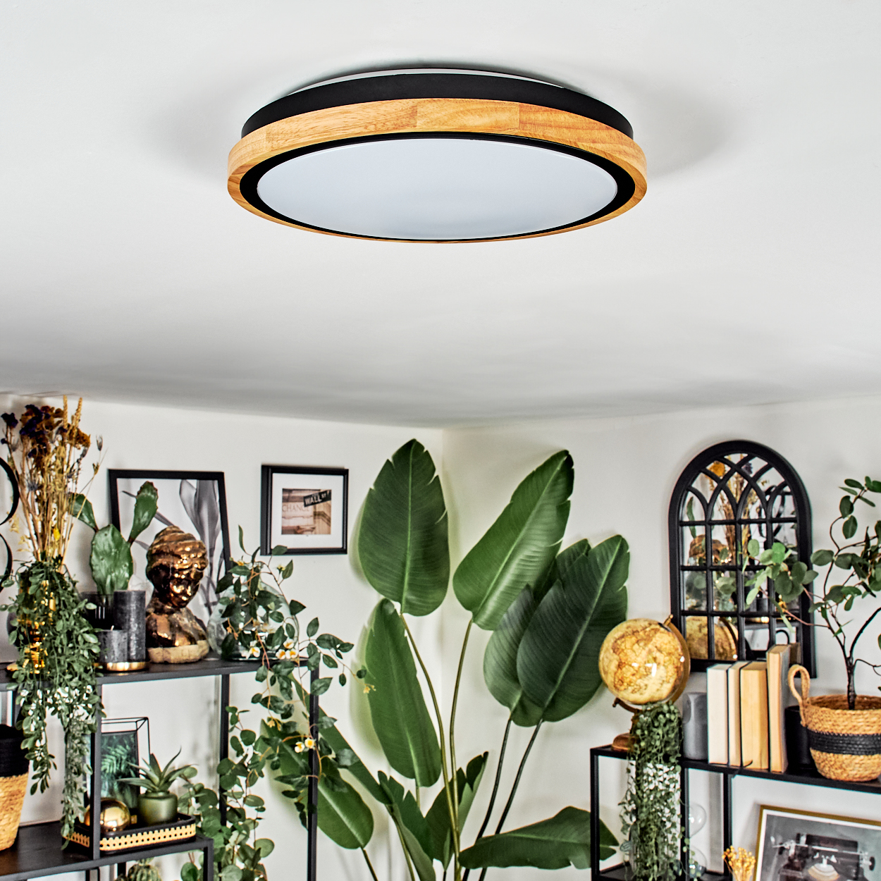 Eine moderne Deckenlampe mit Holzrahmen ist zentriert. Der Raum hat Pflanzen, Dekoration und eine weiße Decke.