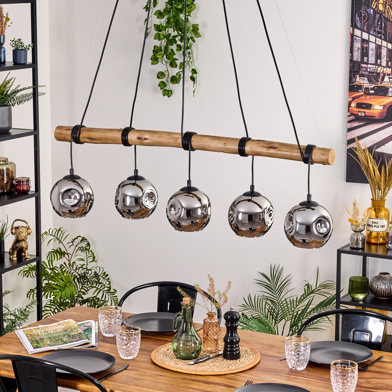 Ein gedeckter Esstisch. Enthält Teller, Gläser und ein Centerpiece. Oben hängt ein Holzbalken mit fünf Kugellampen.