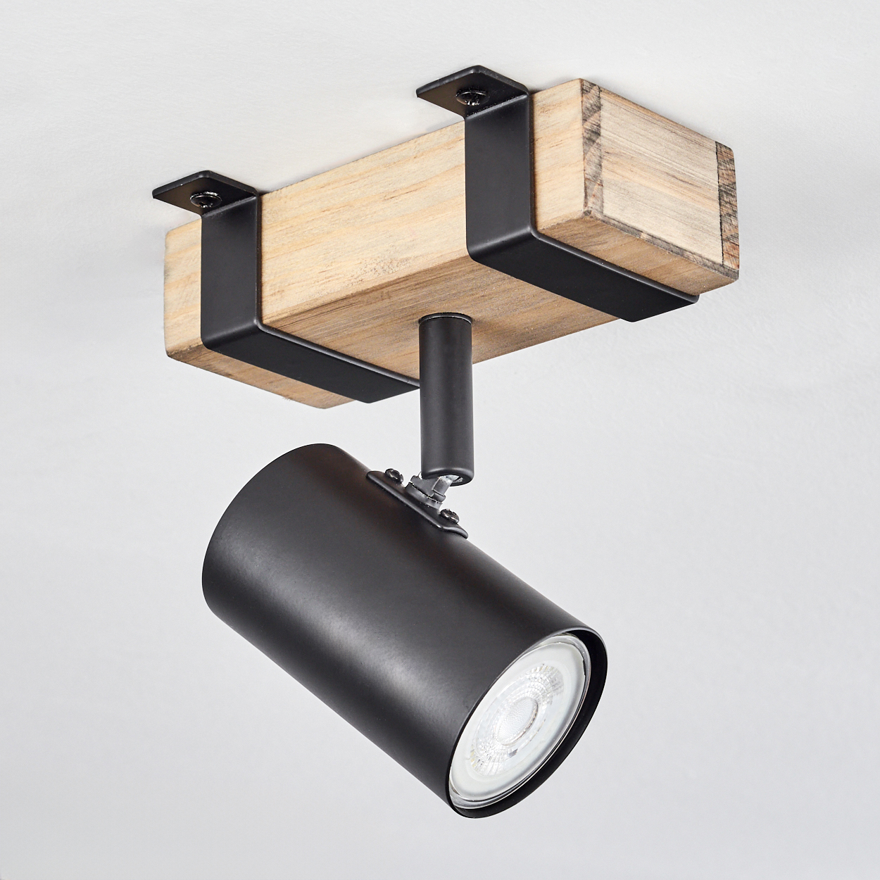 Ein moderner Deckenstrahler. Er hat eine schwarze zylindrische Lampe, die auf einem Holzbalken mit schwarzen Metallbügeln montiert ist.