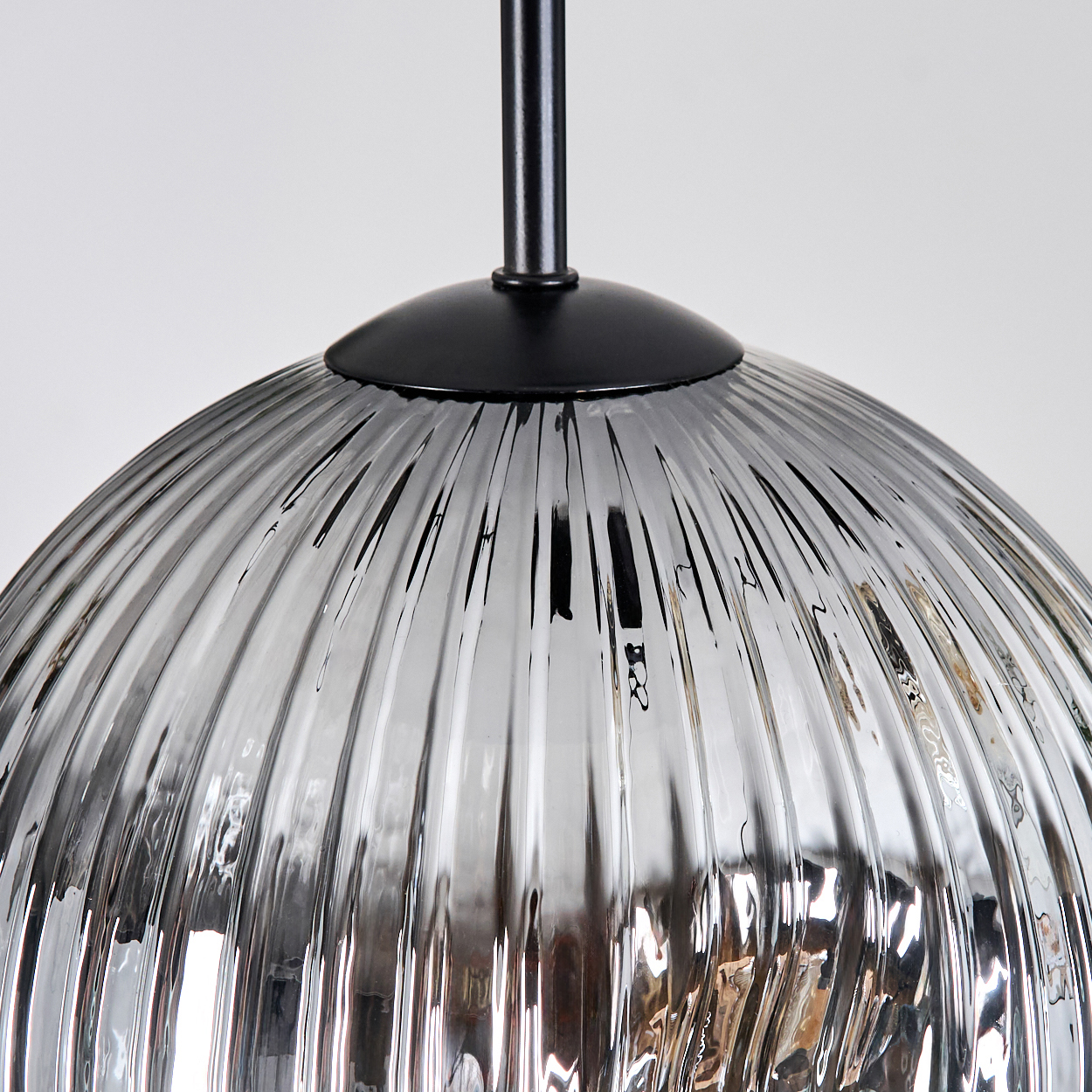 Nahaufnahme eines Lampenschirms aus Glas mit vertikalen Rillen. Ein schwarzer Metallschaft und Baldachin sind oben. Weißer Hintergrund.