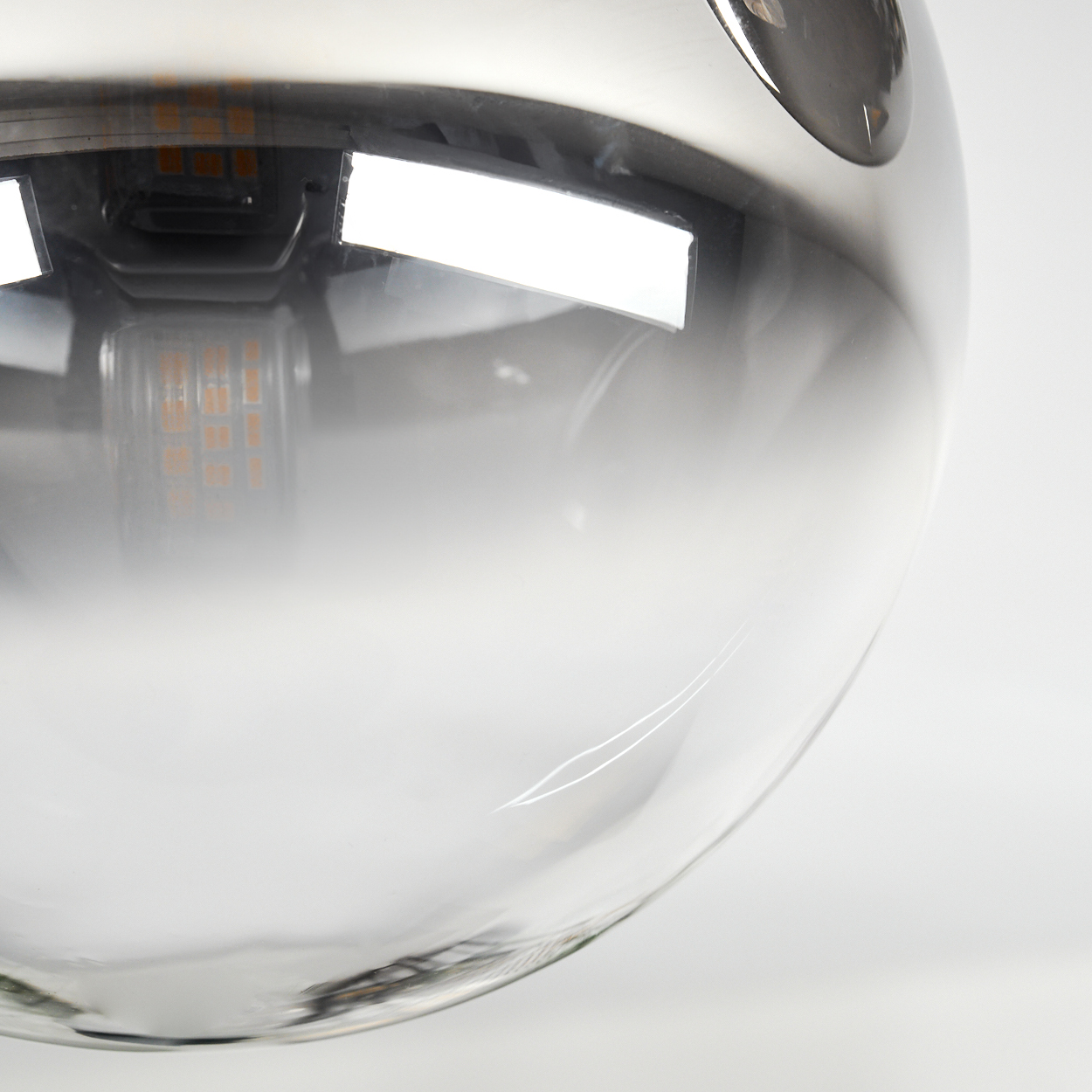 Nahaufnahme einer Glaskugel-Lampe mit metallischem Oberteil. Innen ist eine Lichtquelle mit orangen LEDs sichtbar. Der Hintergrund ist weiß.