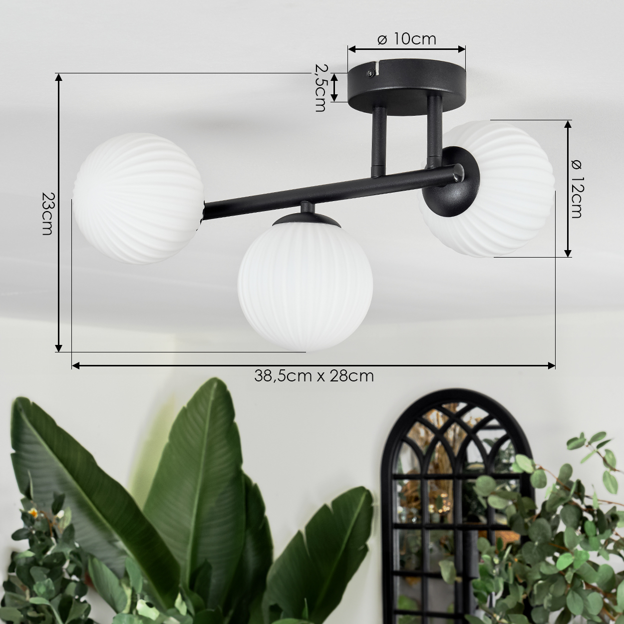 Eine moderne Deckenlampe mit drei weißen, geriffelten Glaskugeln. Schwarzer Metallrahmen. Maße sind angegeben. Grüne Pflanzen und ein Spiegel im Hintergrund.