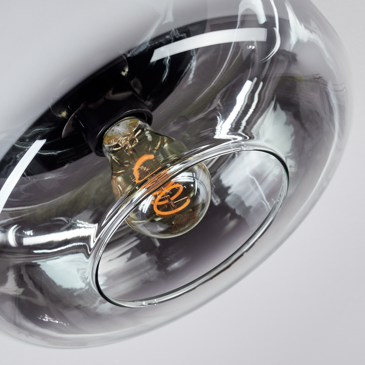 Nahaufnahme einer Leuchte mit rauchigem Glasschirm. Im Inneren befindet sich eine leuchtende Glühbirne mit Spiralfaden.