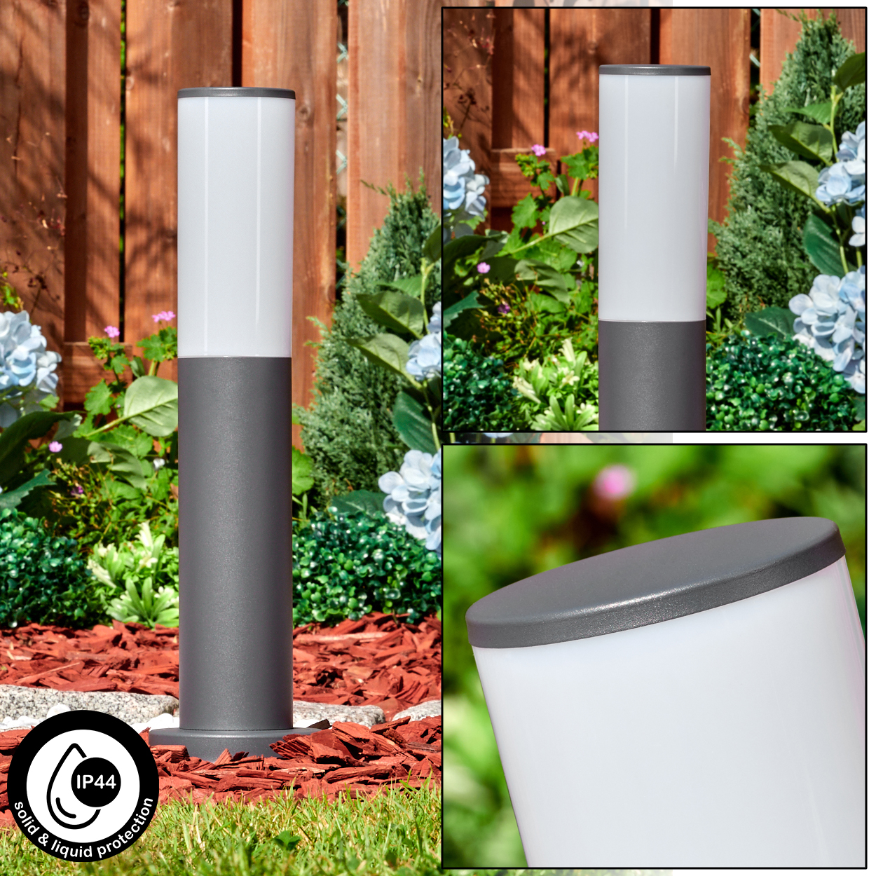 Eine grau-weiße Außenlampe. Sie steht auf Gras, umgeben von Pflanzen und roter Mulch. Der Hintergrund ist ein Holzzaun.