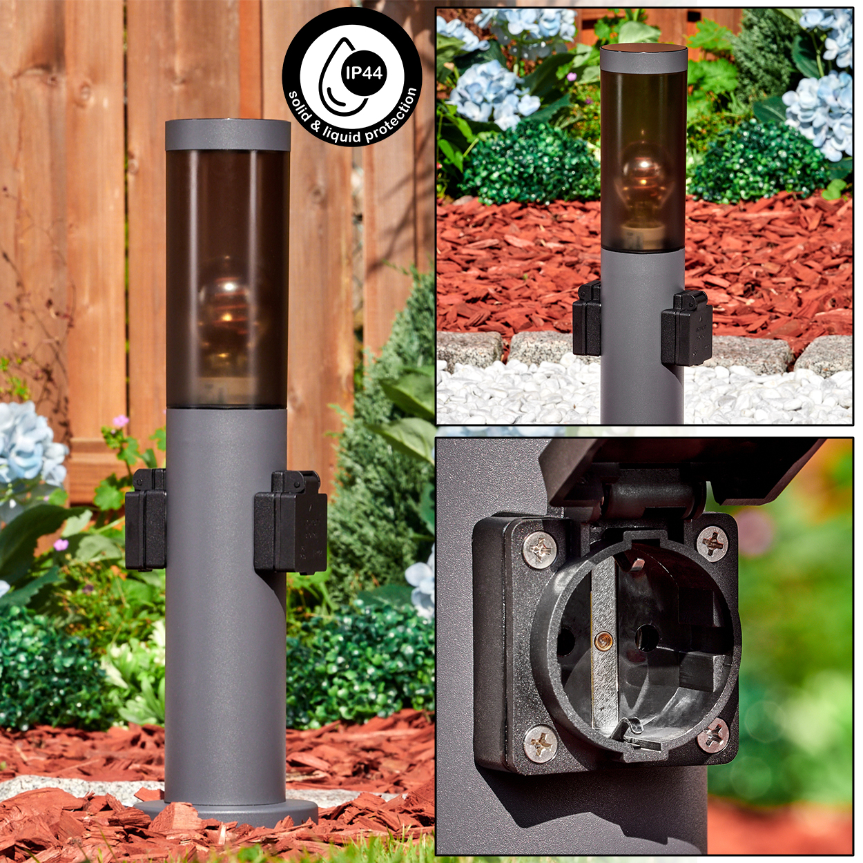 Graue Außenlampe mit Steckdose. Sie hat ein zylindrisches Design. Der Hintergrund zeigt Gartenelemente und Holzzaun.
