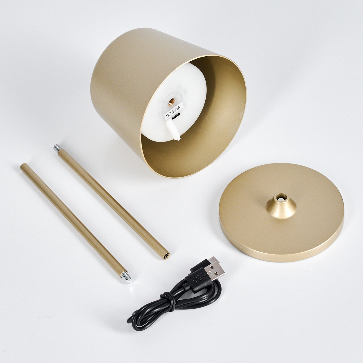 Goldene Kerzenhalterteile: Sockel, Zylinder, zwei Stäbe, USB-Kabel. Weißer Hintergrund. Zylinder hat weißes Innere mit Anschluss.