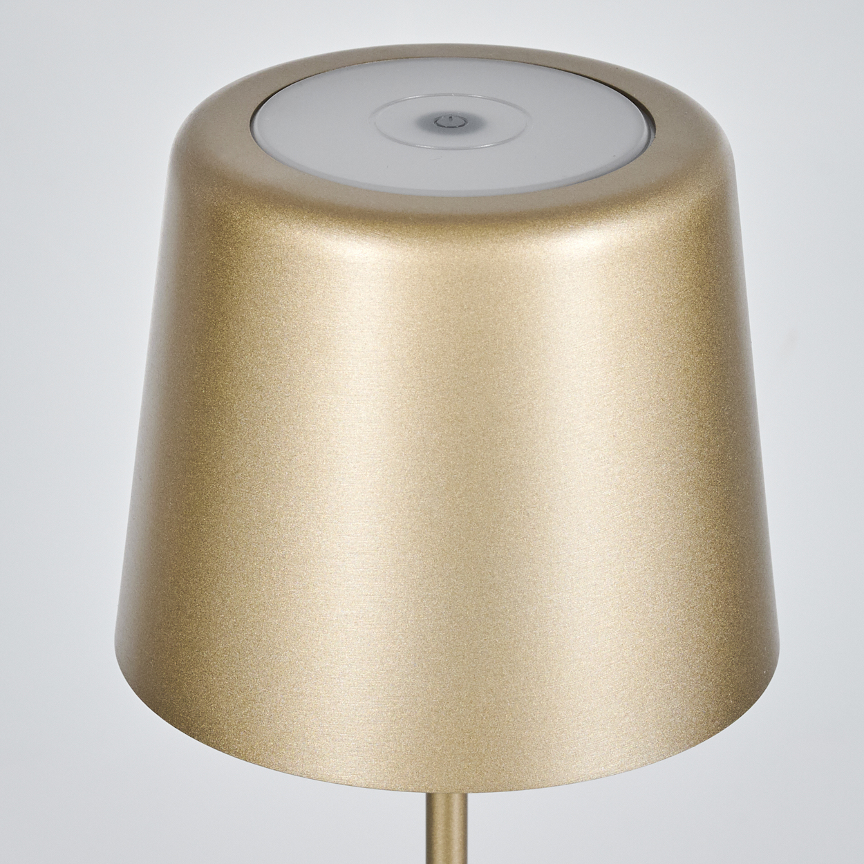 Eine goldene Lampe mit weißer Oberseite. Die Lampe hat eine zylindrische Form und einen Power-Knopf oben.