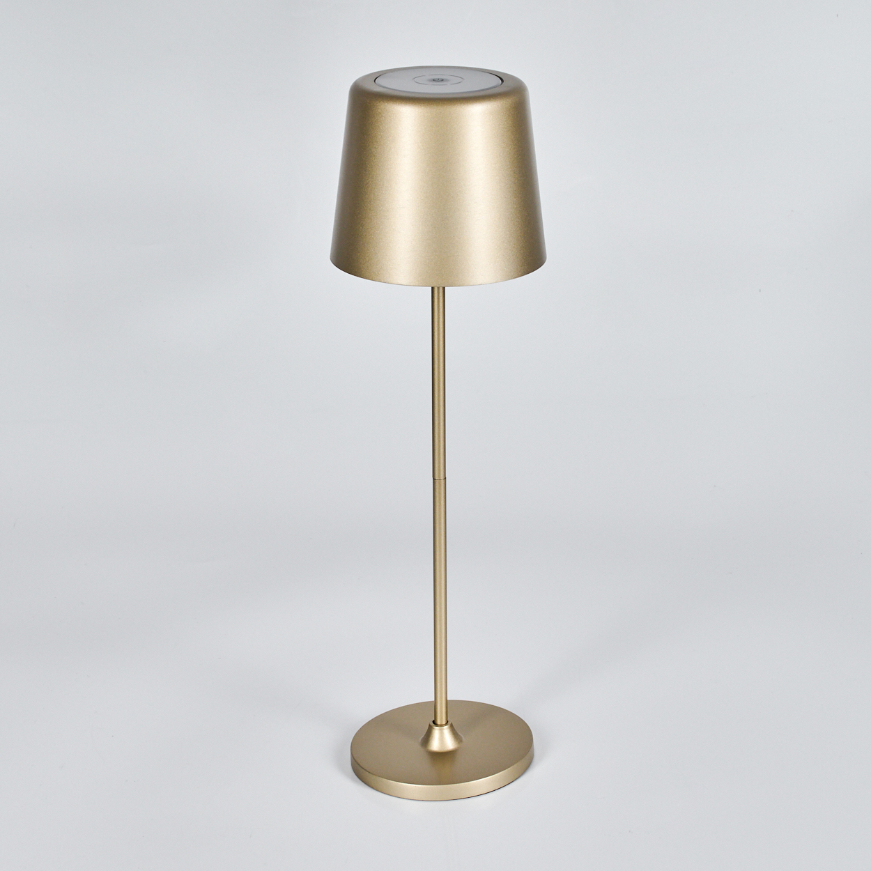 Eine goldene Lampe auf weißem Hintergrund. Sie hat einen runden Fuß, einen dünnen Stiel und einen Lampenschirm, der oben breiter ist.
