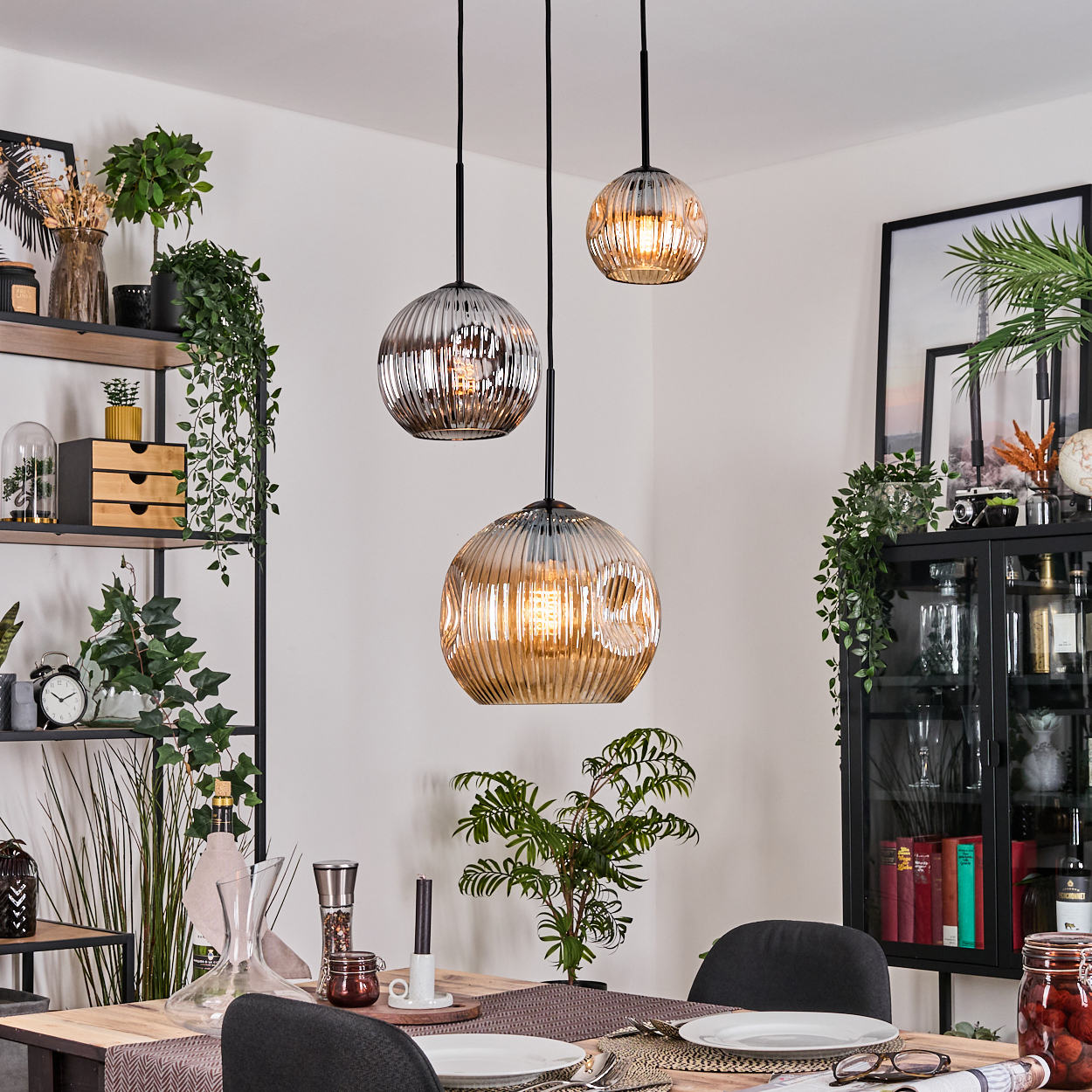 Esszimmer mit drei Hängelampen. Tisch mit Tellern und Gläsern. Pflanzen und Dekorationen im Hintergrund.