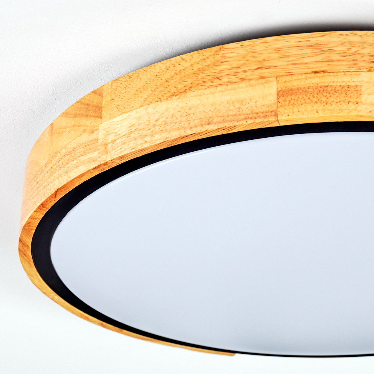 Nahaufnahme einer runden Holzlampe. Sie hat einen hellen Holzrahmen, einen schwarzen Rand und eine weiße, zentrale Lichtplatte.