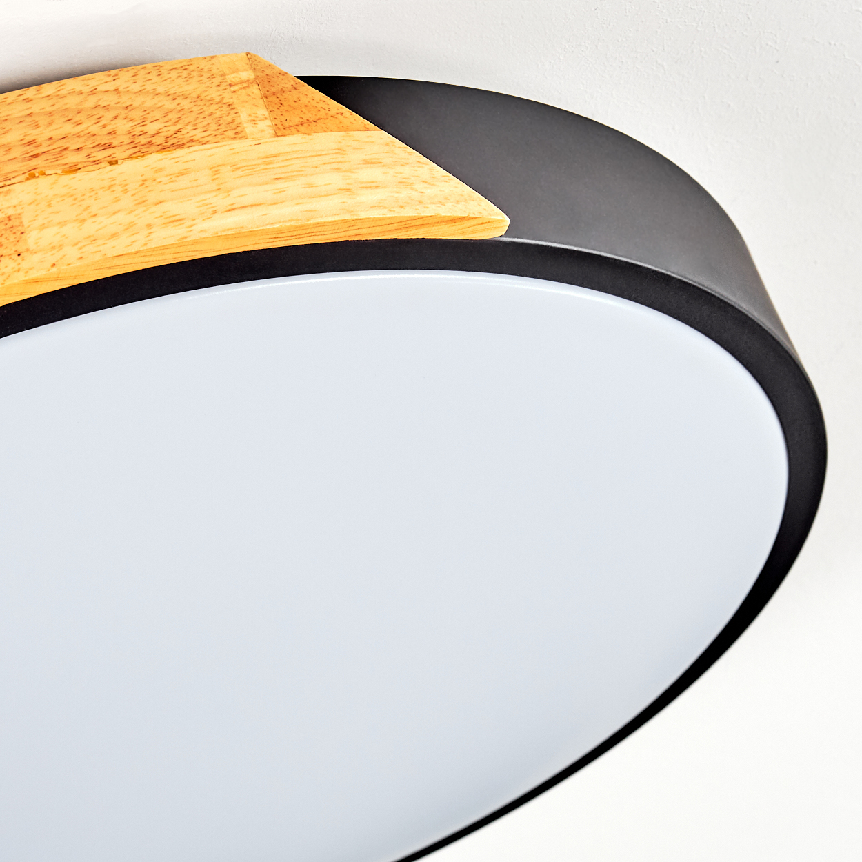 Nahaufnahme einer modernen Deckenleuchte. Sie hat eine Holzverkleidung, einen dunkelgrauen Rand und eine weiße, runde Lichtfläche.