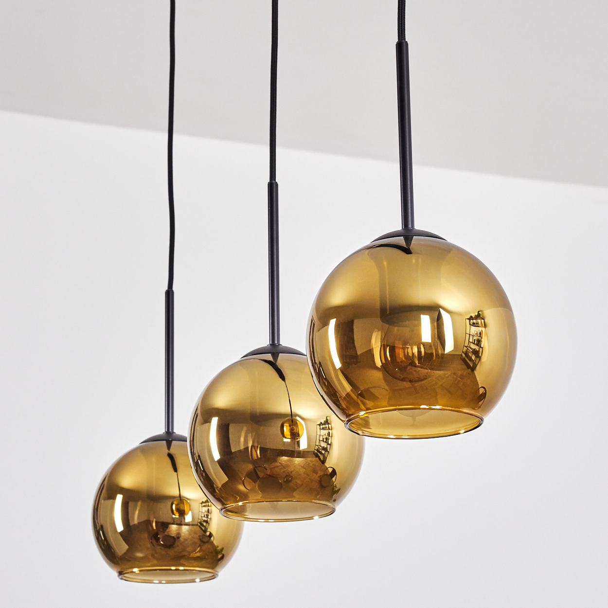 Drei goldene, kugelförmige Pendelleuchten hängen vor einem weißen Hintergrund. Jede hat einen schwarzen Stiel und eine reflektierende Oberfläche.