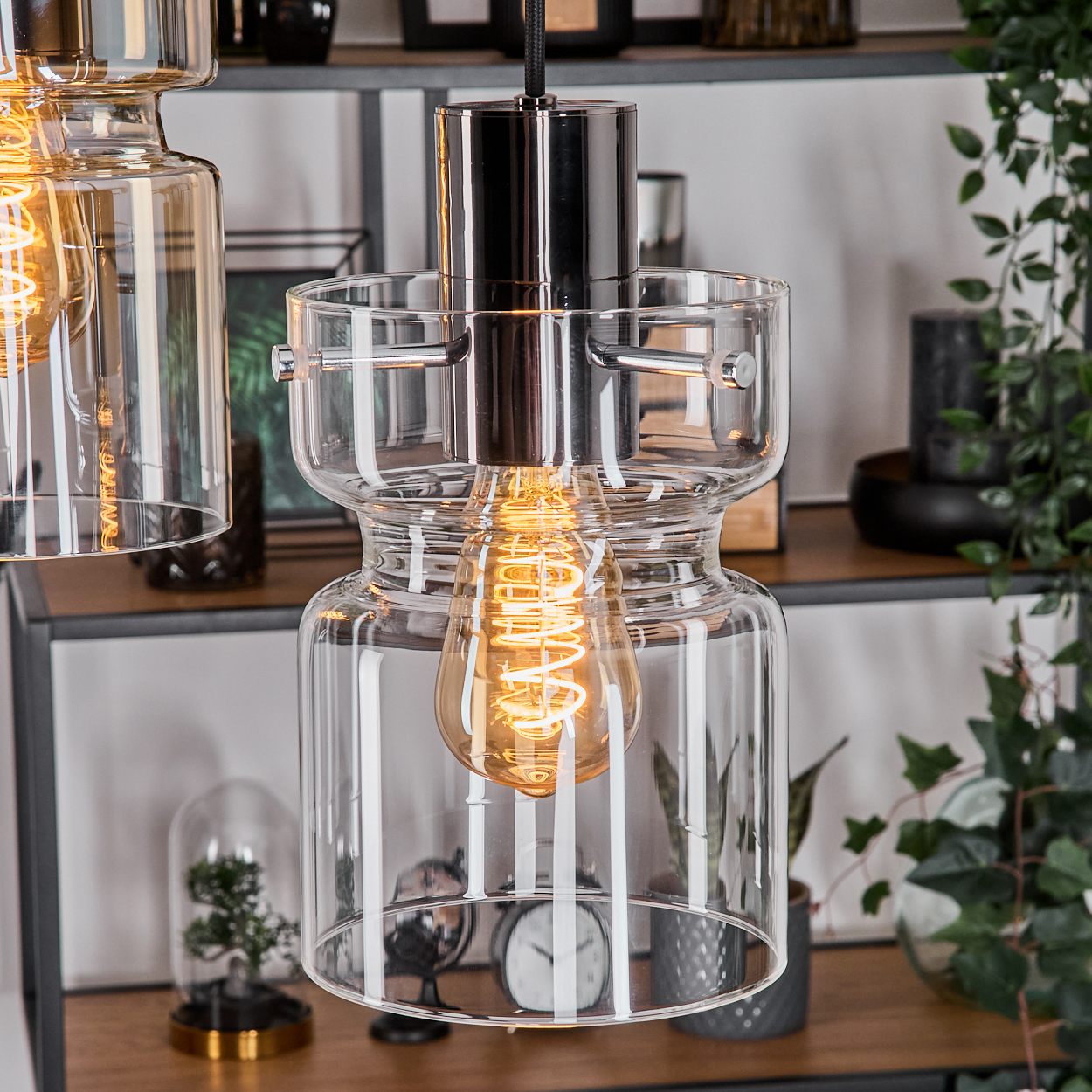 Nahaufnahme von Glas-Pendelleuchten mit glühenden Glühbirnen. Regale im Hintergrund halten Dekoration und Pflanzen.