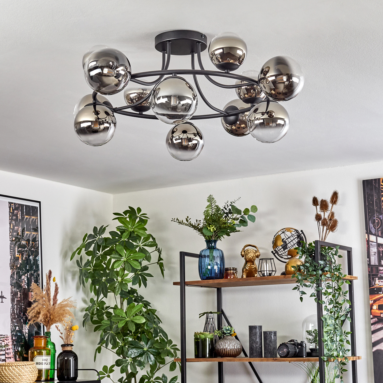 Ein modernes Wohnzimmer mit schwarzer Deckenleuchte, Pflanzen und Regalen. Das Licht hat silberne Kugeln. Pflanzen und Dekoration stehen auf den Regalen.