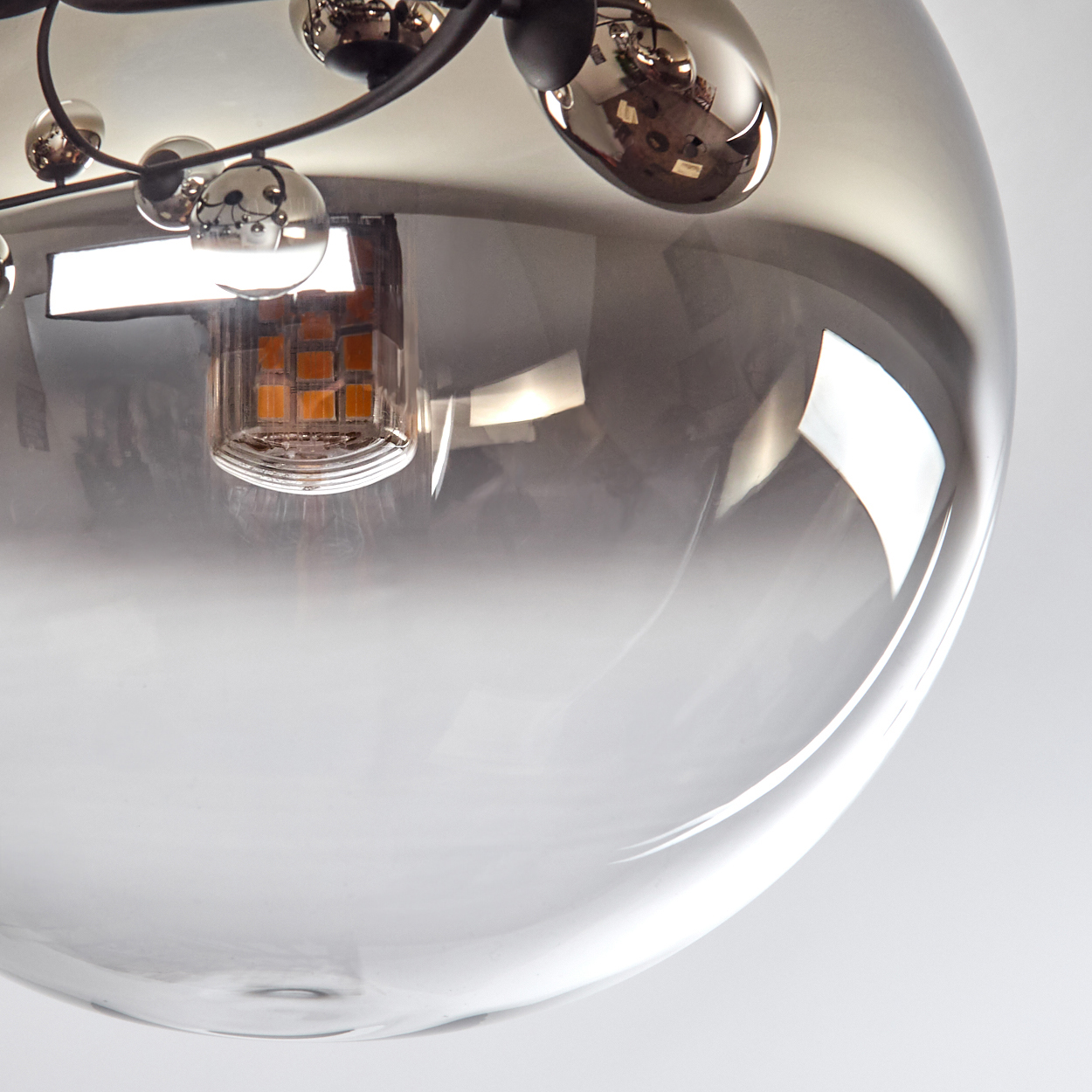 Nahaufnahme einer Glaskugelleuchte. Sie hat eine reflektierende Oberfläche und einen schwarzen Metallrahmen. Innen ist eine Glühbirne sichtbar.