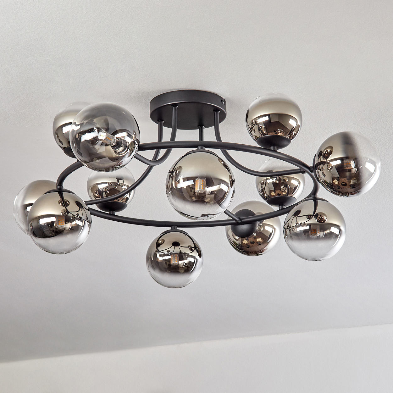 Eine moderne Deckenleuchte mit schwarzem Rahmen und mehreren reflektierenden, rauchgrauen Glaskugeln.