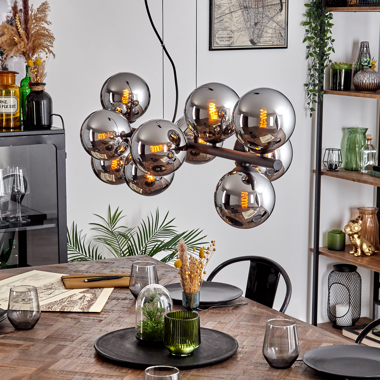 Esszimmer mit Holztisch, rundem Kronleuchter, Gläsern, Tellern und Dekorationen. Rechts ein schwarzer Stuhl.