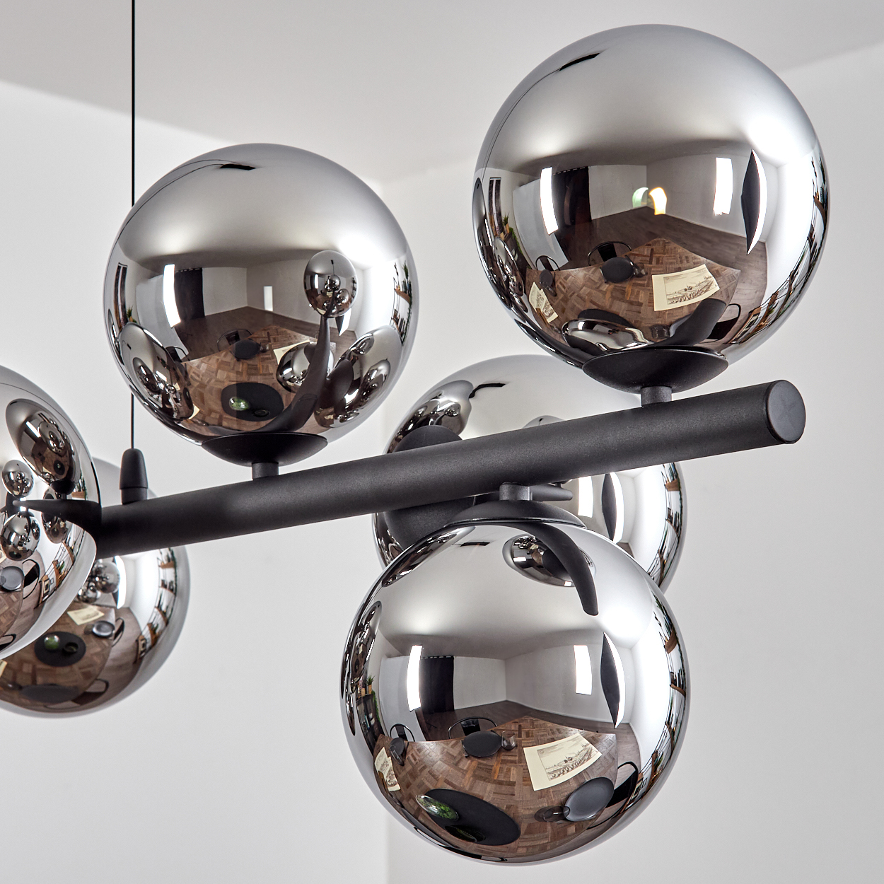 Eine moderne Chrom-Deckenleuchte mit kugelförmigen Lichtern reflektiert den Raum. Die Leuchte ist schwarz und an einer weißen Decke montiert.