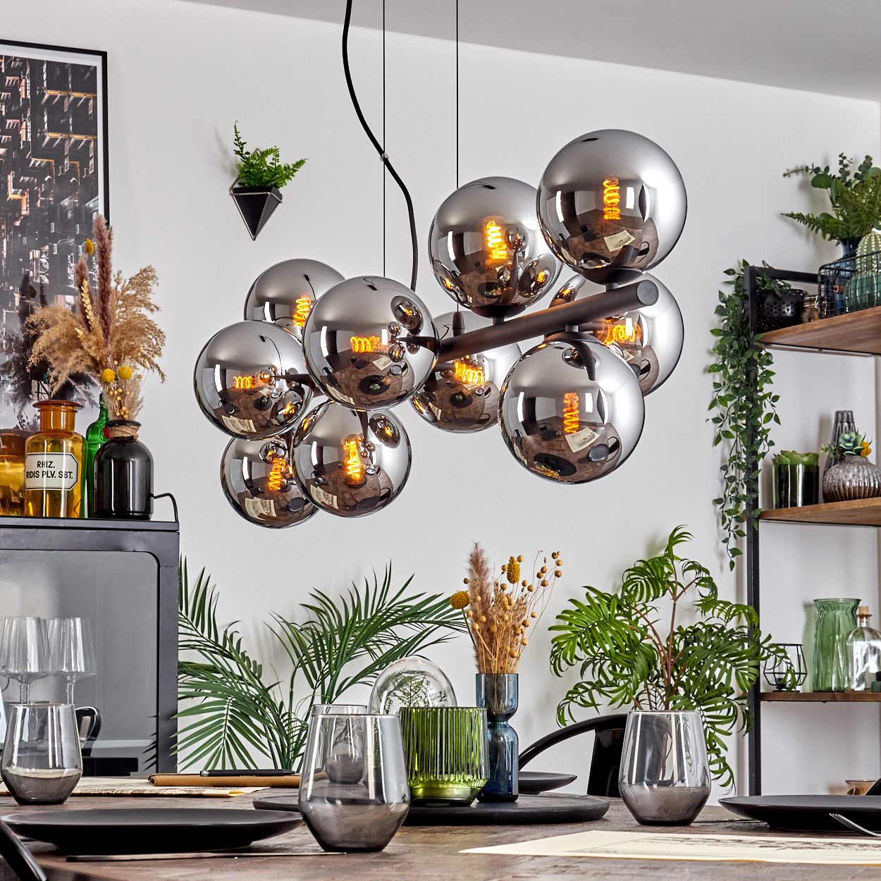 Ein Esszimmer mit einem verspiegelten Kronleuchter. Pflanzen und Gläser stehen auf dem Tisch. Regale mit Pflanzen und Dekoration sind sichtbar.