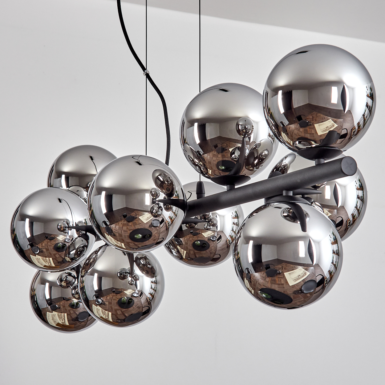 Ein moderner Kronleuchter mit mehreren glänzenden silbernen Kugeln, die den Raum reflektieren. Die Kugeln sind an einem schwarzen Rahmen befestigt.