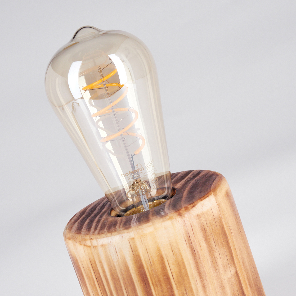 Nahaufnahme einer Glühbirne in einem Holzsockel. Die Birne ist aus Glas mit sichtbarem Glühfaden. Der Sockel ist braunes Holz.