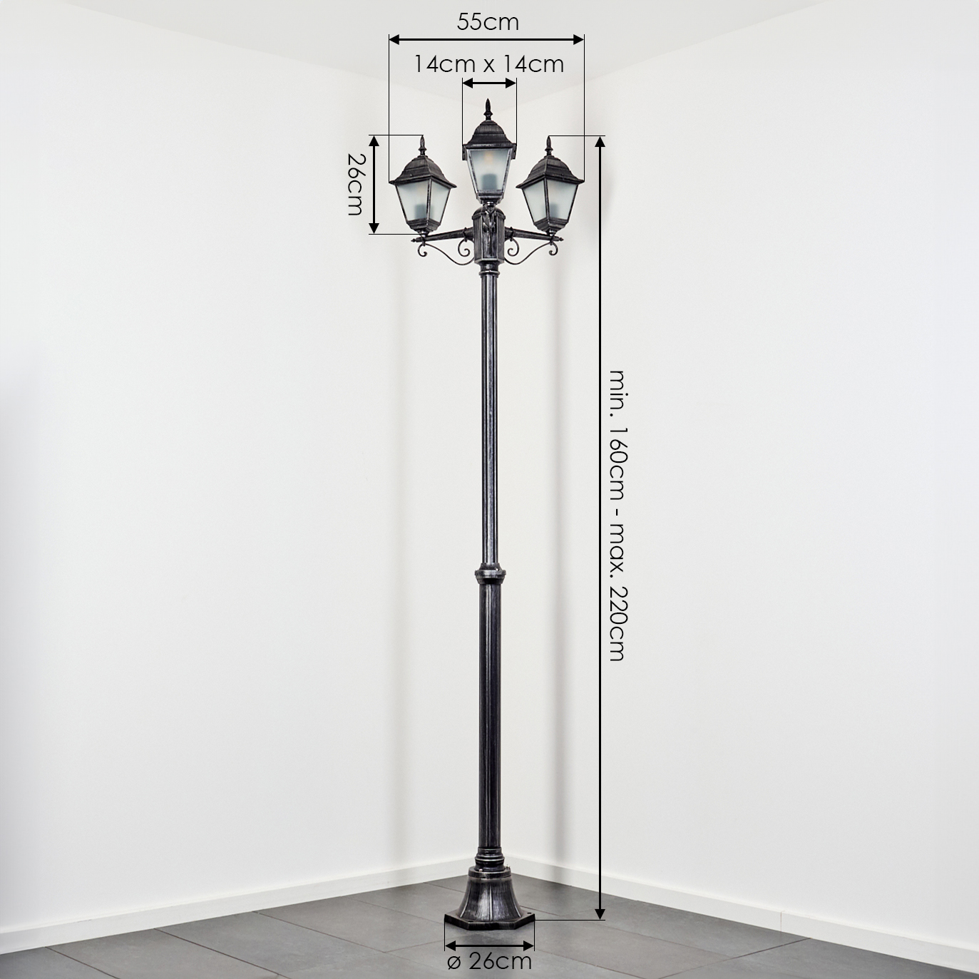 Eine schwarze Straßenlaterne mit drei Lichtern steht in der Ecke eines weißen Raumes. Maße sind angegeben. Die Lampe steht auf einem gefliesten Boden.