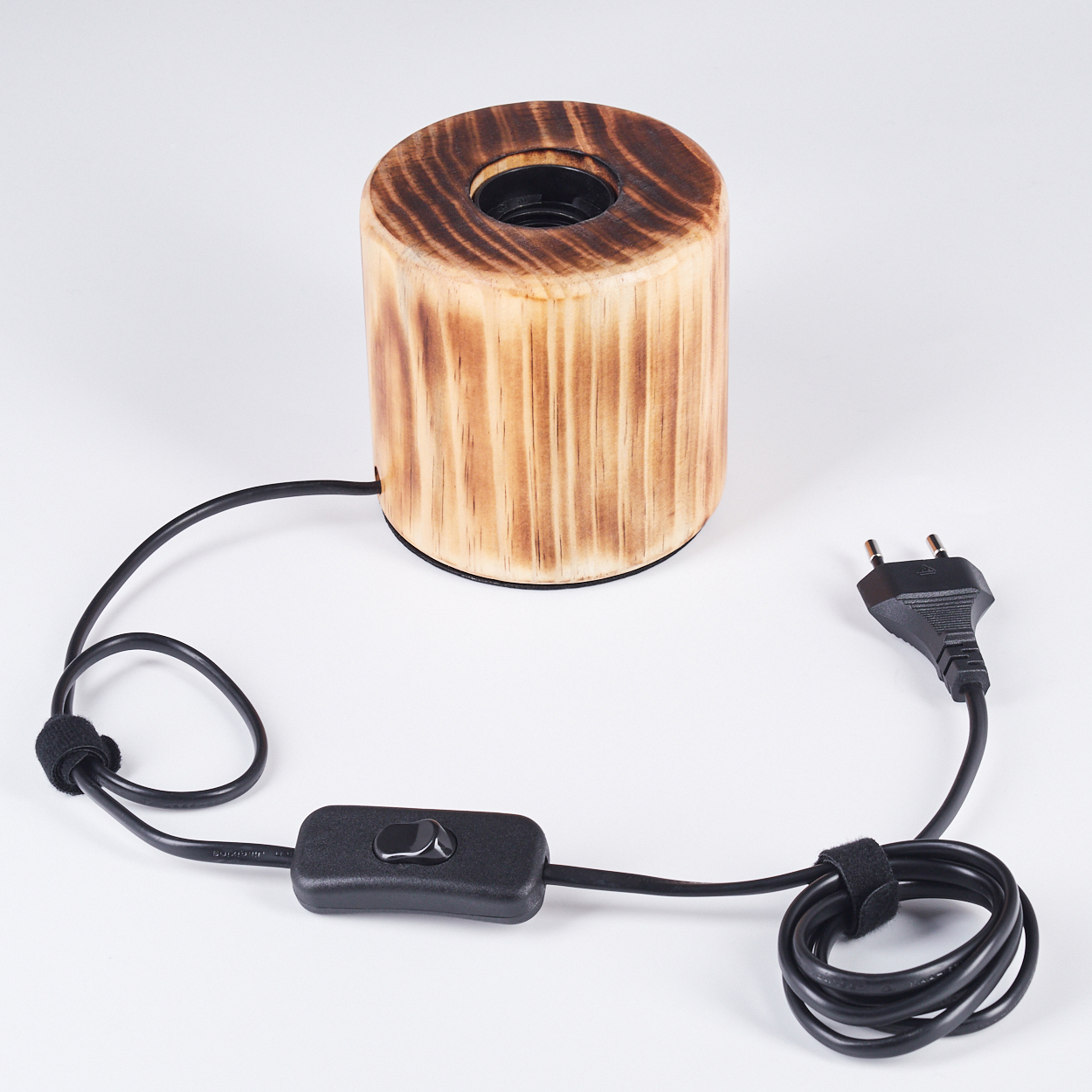 Holzlampe mit schwarzem Kabel, Schalter und Stecker auf weißem Untergrund. Die Lampe ist zylindrisch mit dunkler Oberseite.