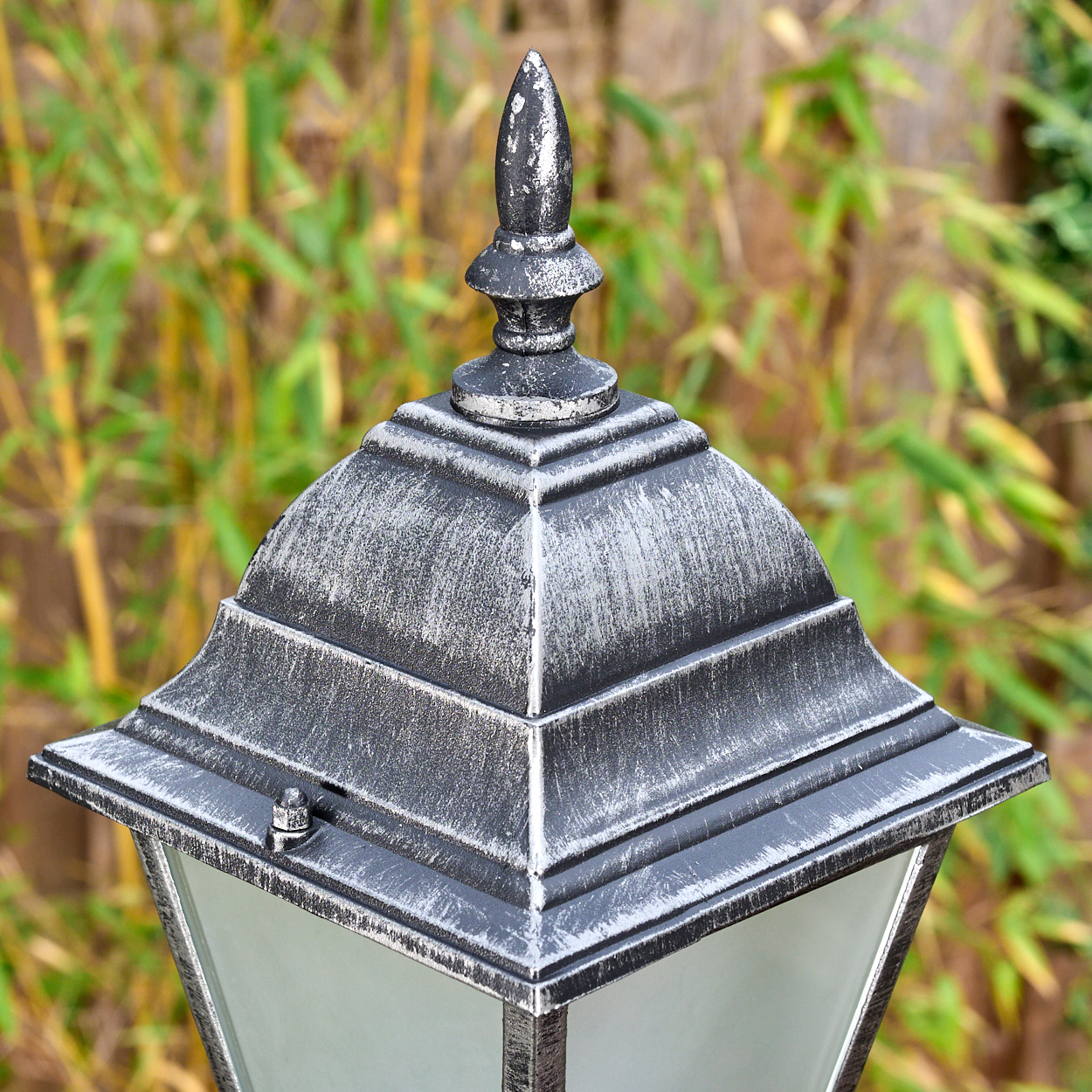 Nahaufnahme einer dekorativen Außenlampe mit silberner und schwarzer Oberfläche. Bambusbäume im verschwommenen Hintergrund.