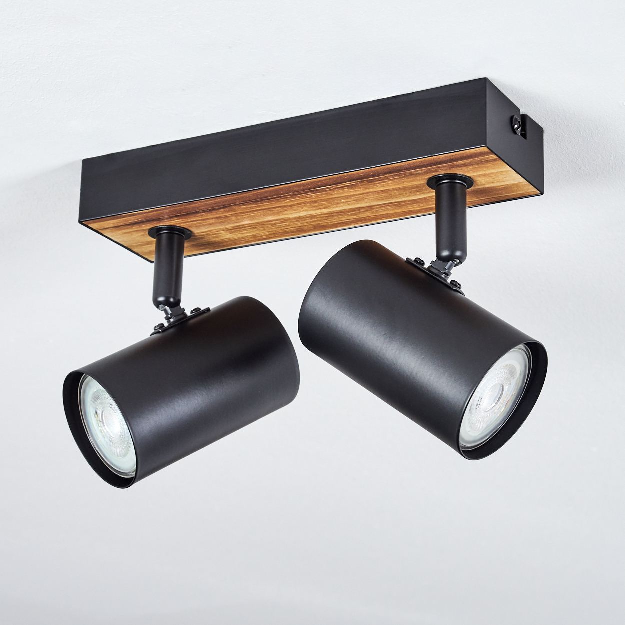 Moderne Deckenstrahler. Es hat zwei schwarze zylindrische Lichter, die an einer Holzbasis befestigt sind. Der Hintergrund ist weiß.