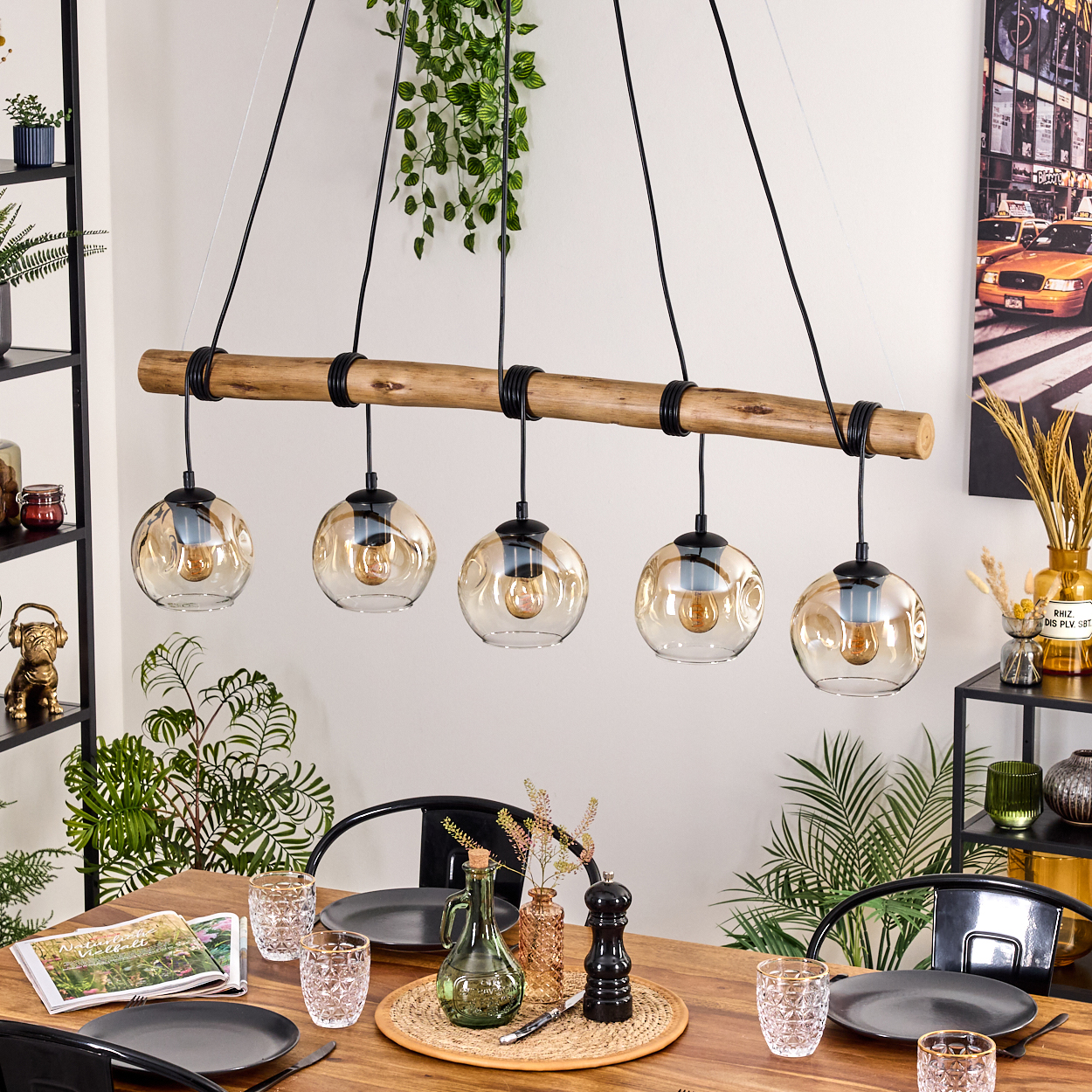 Esszimmer mit Holztisch, schwarzen Stühlen und Kronleuchter mit fünf Glaskugelleuchten. Pflanzen und Dekorationen.