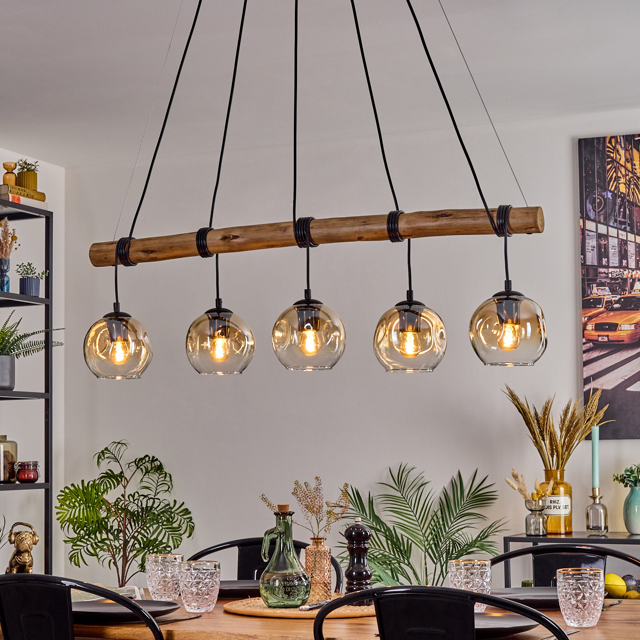 Ein Esszimmer mit Holztisch, schwarzen Stühlen und einer Leuchte mit fünf Glaskugelleuchten. Pflanzen und Dekorationen.