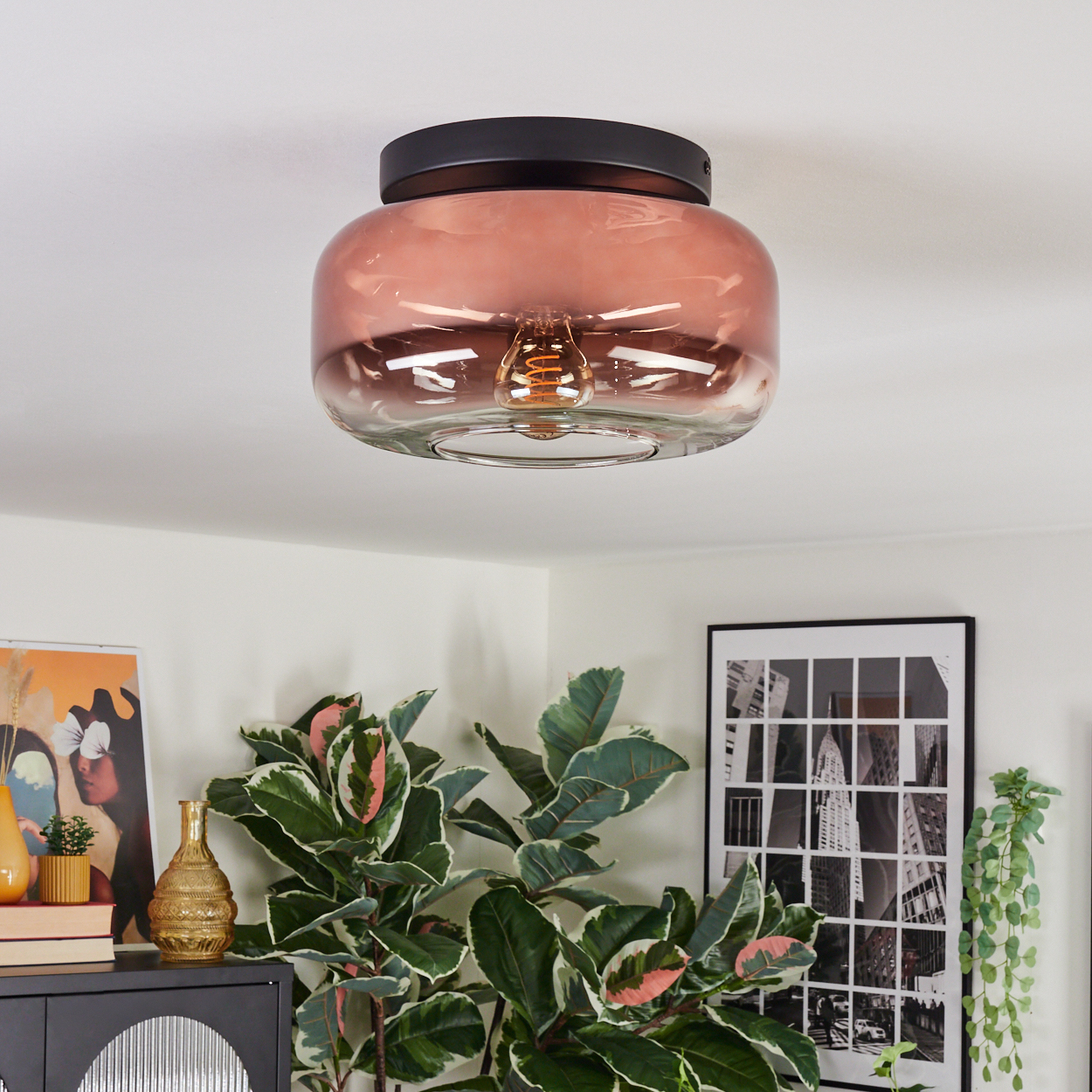 Eine moderne Deckenleuchte mit rosafarbenem Glasschirm. Der Raum hat Pflanzen und Kunstwerke. Die Lampe befindet sich an einer weißen Decke.