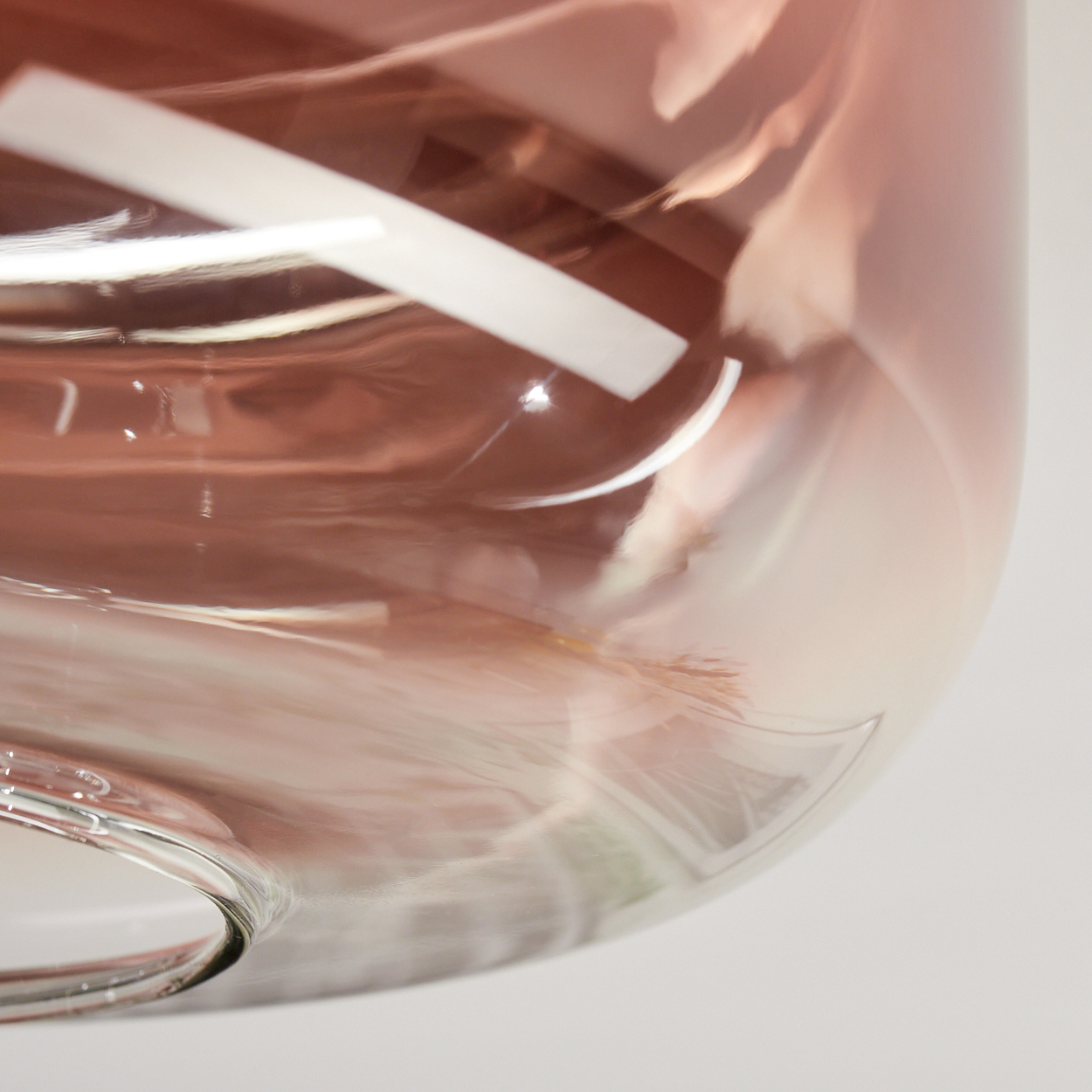 Nahaufnahme eines Glasobjekts. Teilweise transparent, mit rosa und weißen Farbverläufen. Ein weißes Etikett ist im Glas sichtbar.