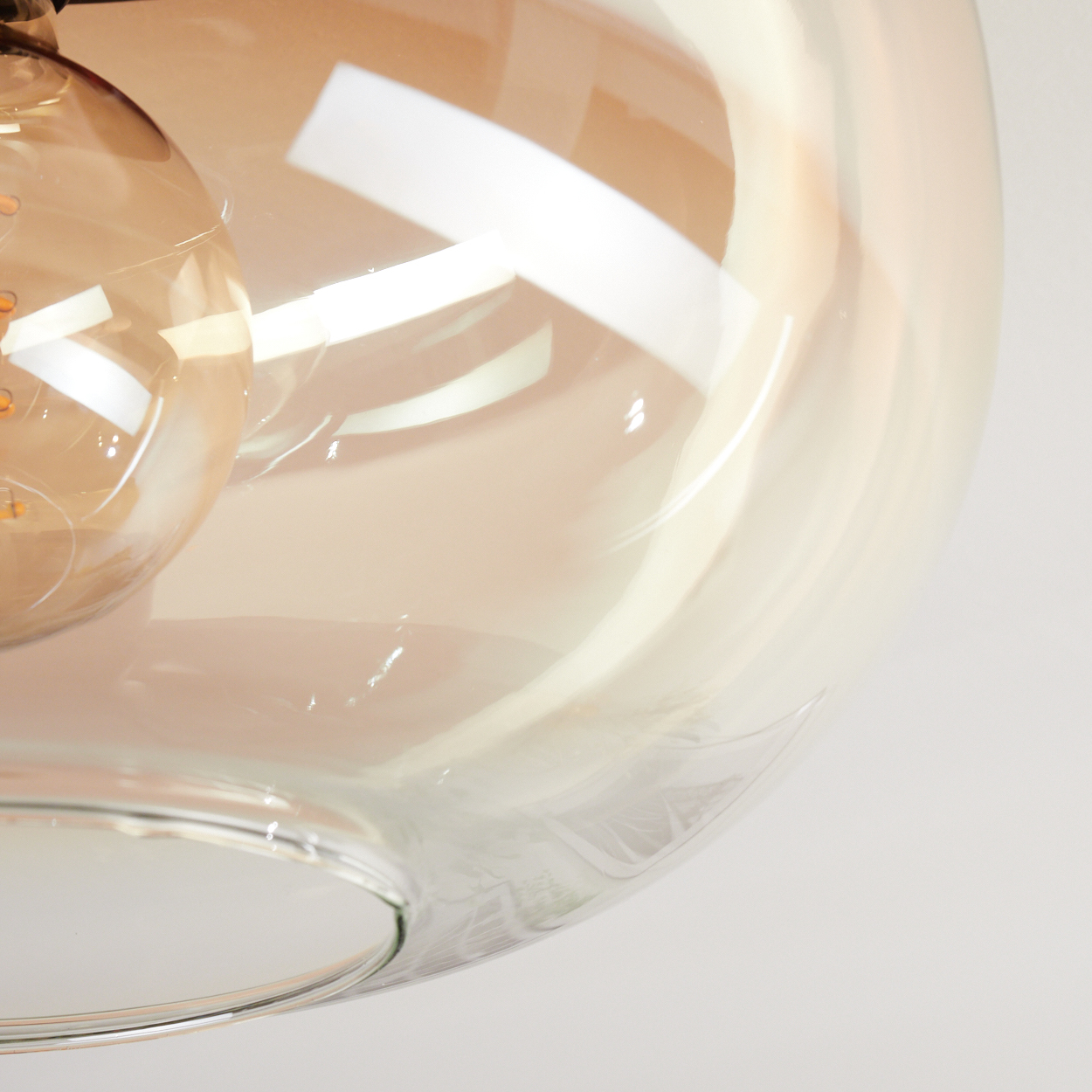 Nahaufnahme einer Glasleuchte, eine Glühbirne sichtbar. Das Glas hat einen klaren, leicht bernsteinfarbenen Ton. Weißer Hintergrund.