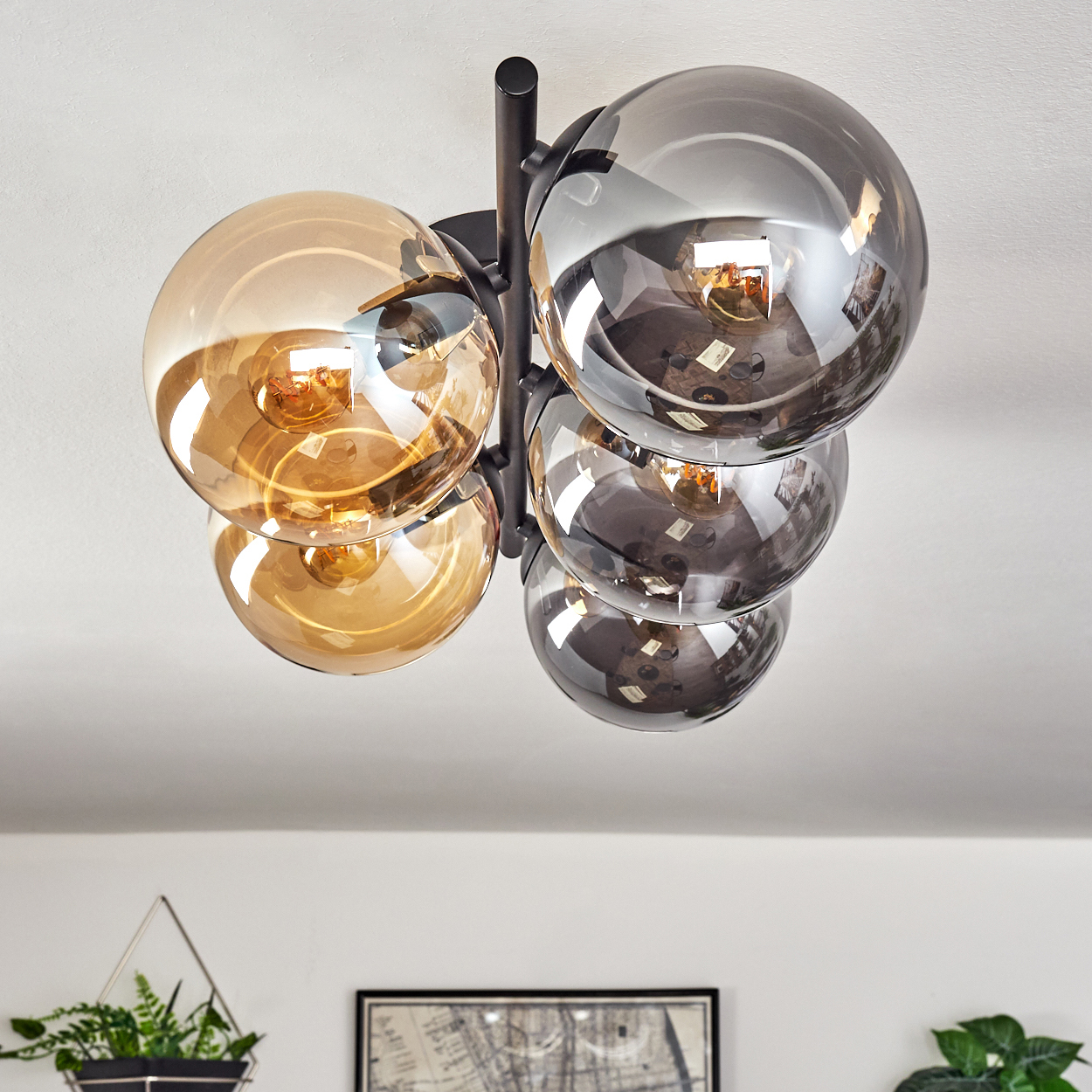 Moderne Deckenleuchte mit kugelförmigen Glasschirmen in Bernstein und Silber. Sie hängt an einem schwarzen Metallrahmen.