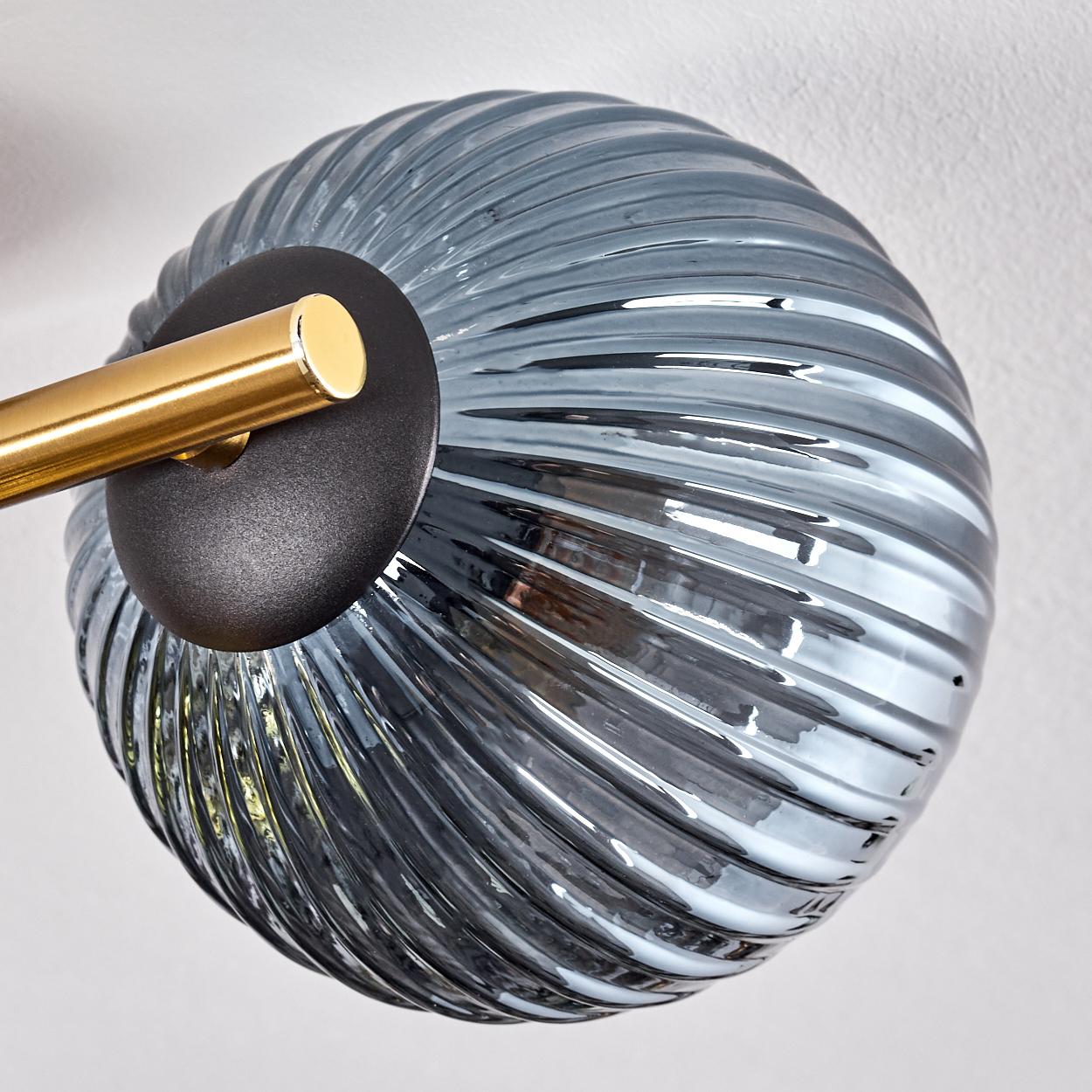 Nahaufnahme einer Lampe. Sie hat einen blau gewirbelten Glasschirm, einen goldfarbenen Metallarm und einen schwarzen Sockel auf weißem Hintergrund.