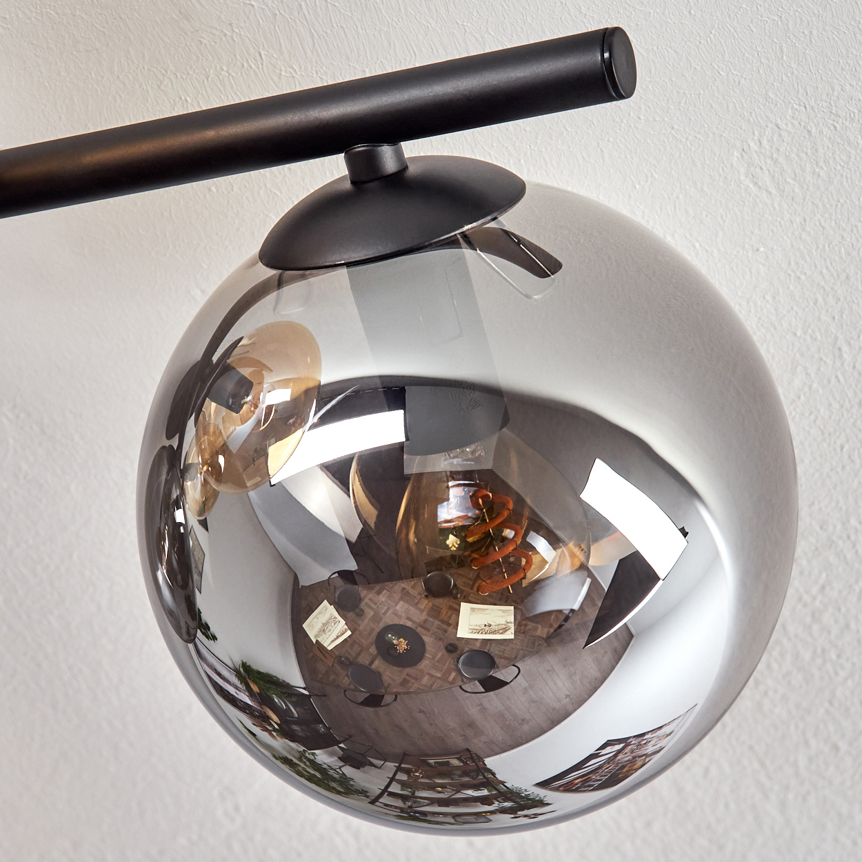 Eine moderne Lampe mit einer reflektierenden Glaskugel, die die Reflexion eines Raumes zeigt. Die Lampe ist schwarz, der Hintergrund ist weiß.