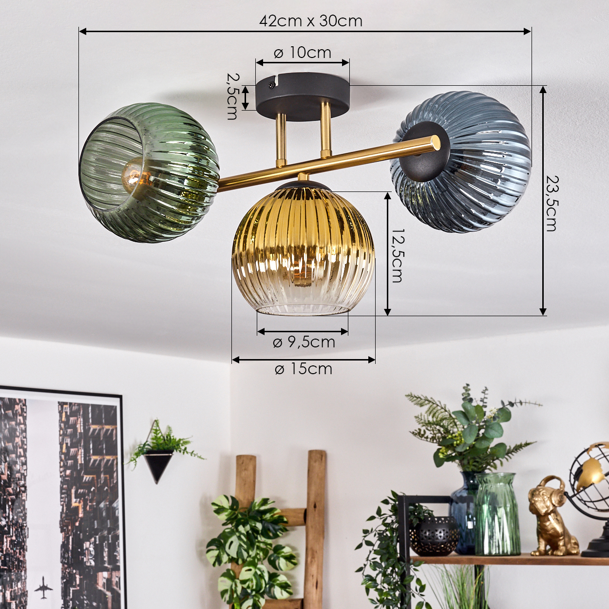 Deckenlampe mit drei Glasschirmen in Grün, Gold und Grau. Maße sind enthalten. Im Hintergrund ein Regal mit Dekoration.