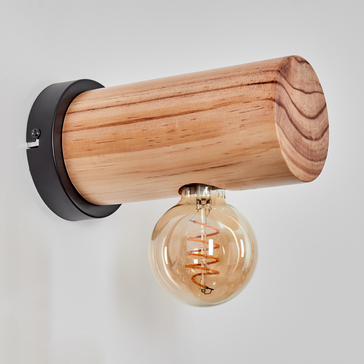 Eine Wandlampe aus Holzbalken mit einer runden, warm getönten Glühbirne hängt an einer weißen Wand. Die Lampe hat eine schwarze Metallhalterung.