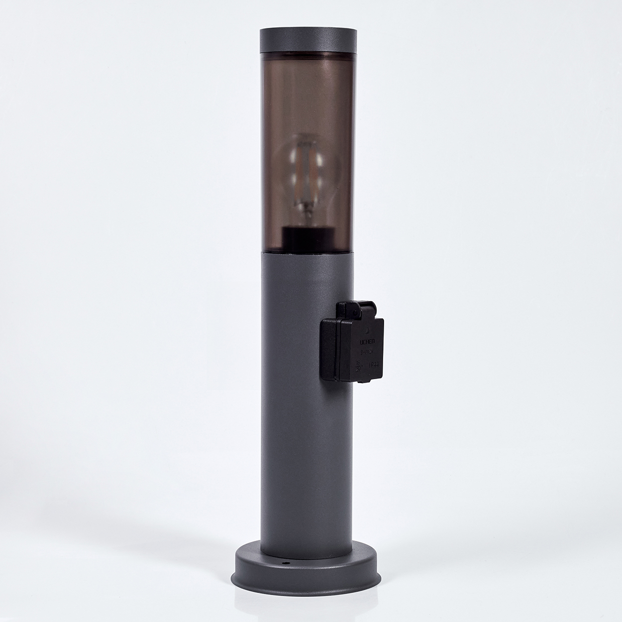 Eine graue zylindrische Lampe mit einem dunklen, durchscheinenden oberen Abschnitt, der eine Glühbirne enthält. An der Seite befindet sich eine schwarze Steckdose.