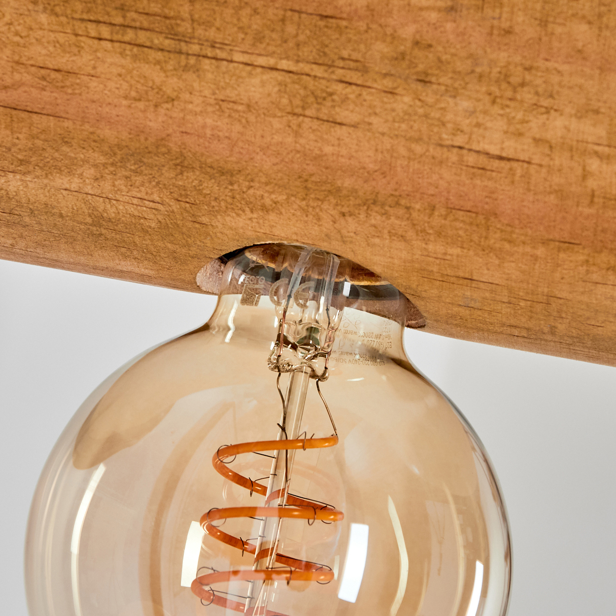 Nahaufnahme einer Glühbirne mit einem Holzbalken darüber. Die Glühbirne ist aus Glas mit einem orangefarbenen Wendel.