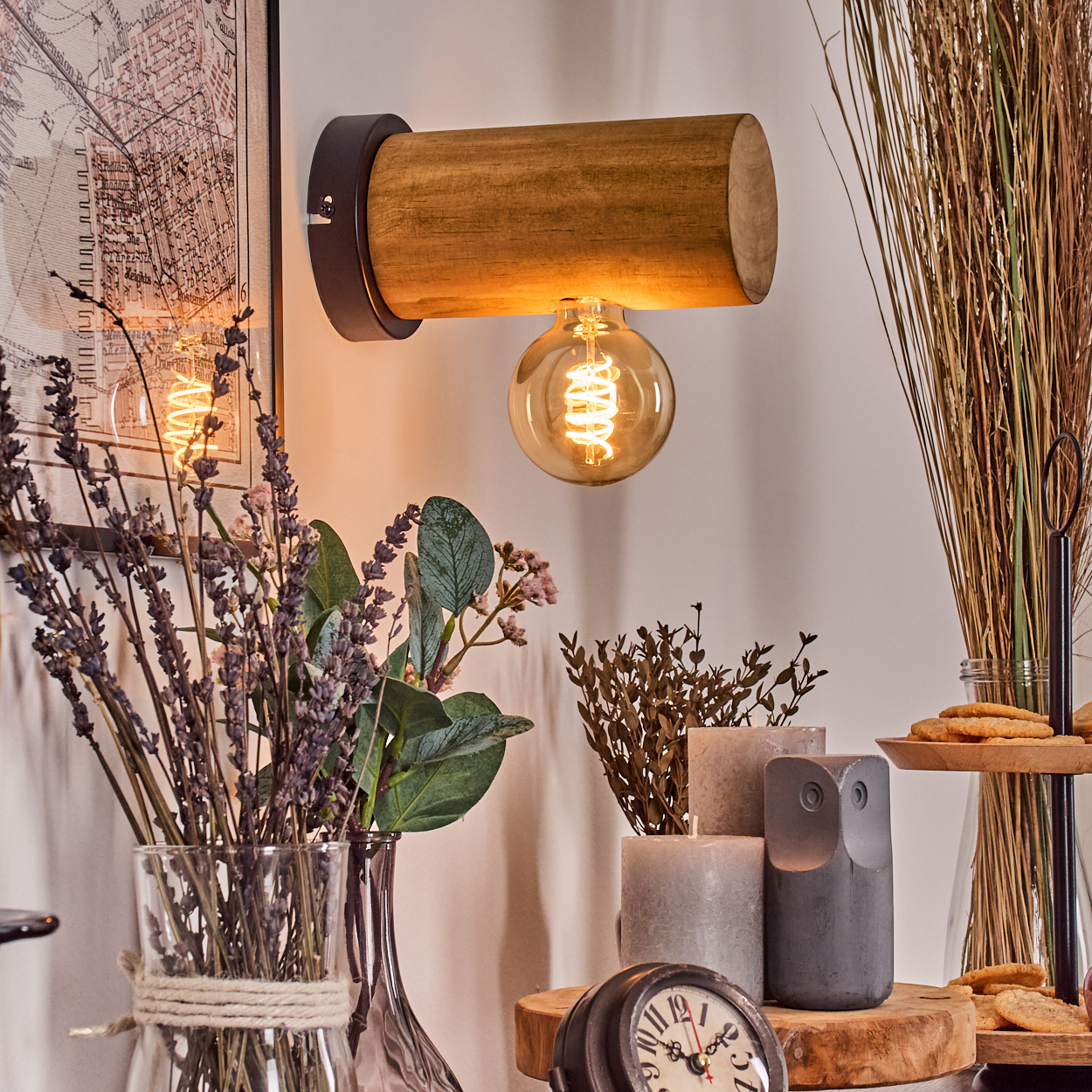 Eine Holzlampe mit leuchtender Glühbirne. Vasen mit Blumen und eine Eulenstatue stehen davor. Kekse auf einem Holzbrett im Hintergrund.