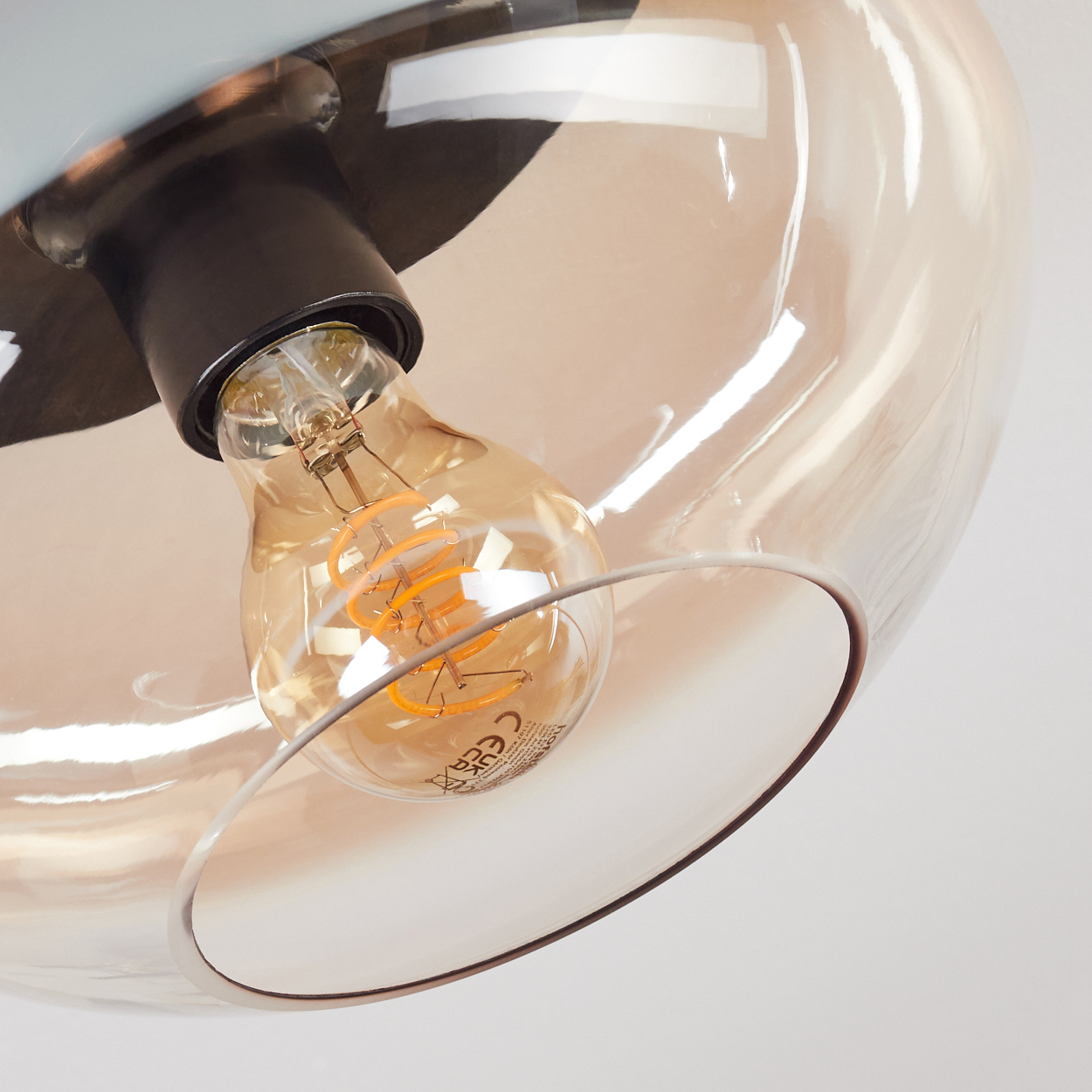 Nahaufnahme einer Leuchte mit tropfenförmigem Glasschirm. Im Inneren befindet sich eine Glühbirne, und die Leuchte befindet sich vor weißem Hintergrund.