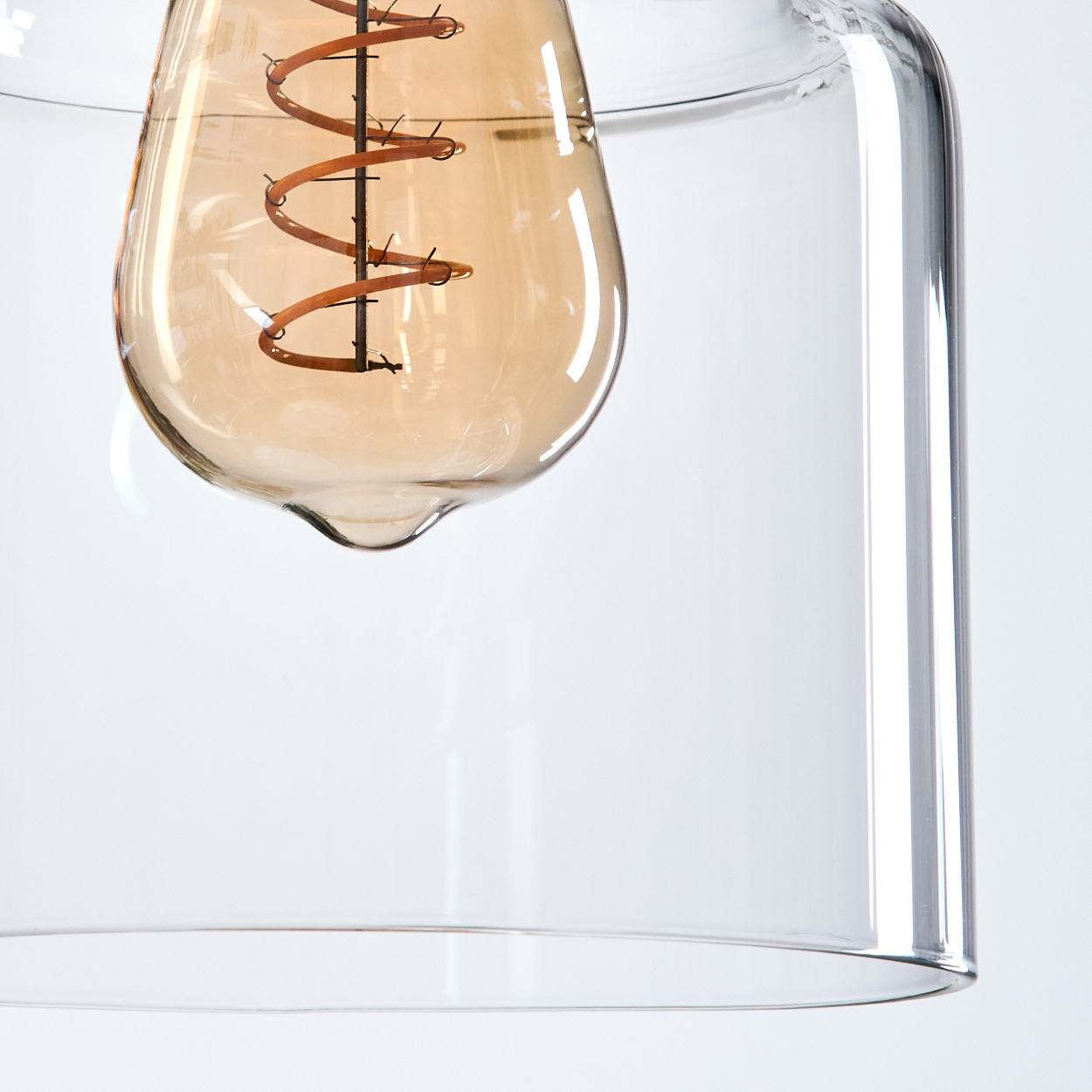 Nahaufnahme einer Glühbirne in einem Glaslampenschirm. Die Birne hat einen kupferfarbenen Wendelfaden. Glas ist klar.
