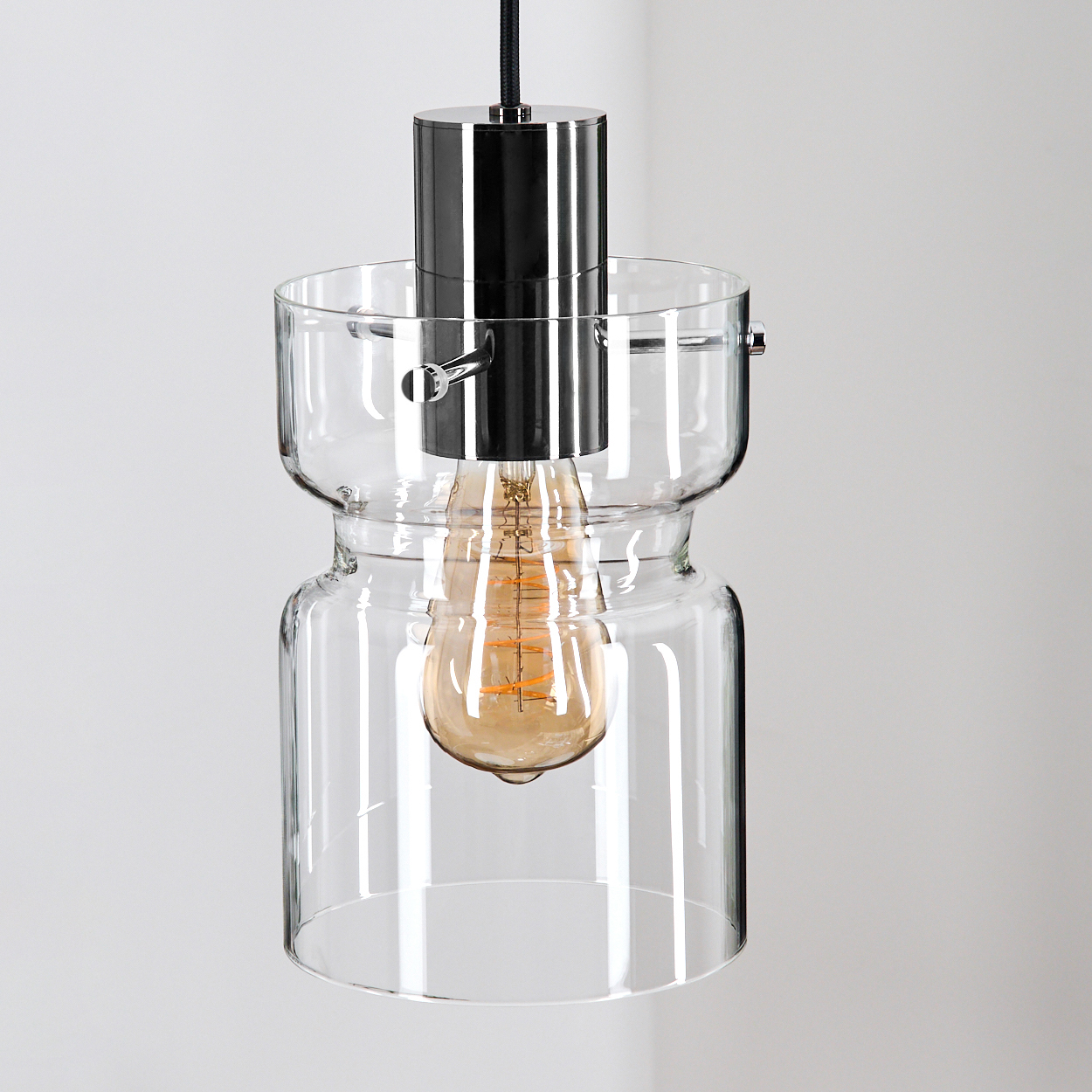 Eine moderne Glas-Pendelleuchte mit Chromaufsatz und sichtbarer Glühbirne. Der Hintergrund ist eine schlichte, weiße Wand.