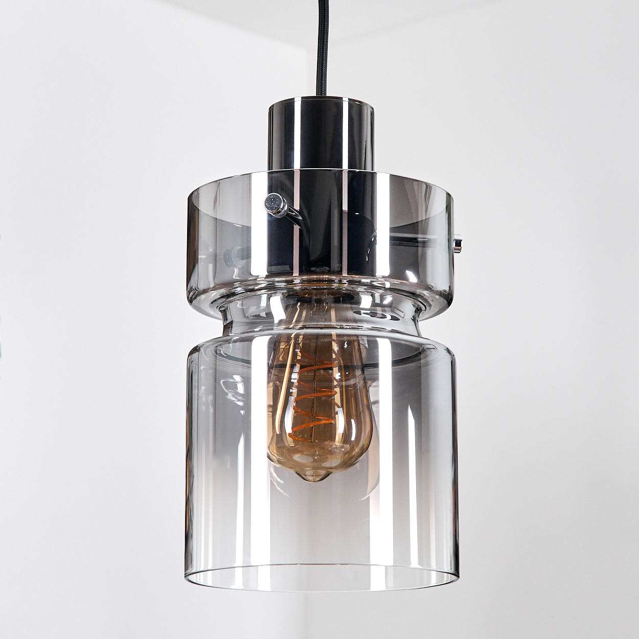 Eine moderne Pendelleuchte mit verchromtem Oberteil und Glasschirm. Die Glühbirne im Inneren ist sichtbar und wirft ein warmes Licht.