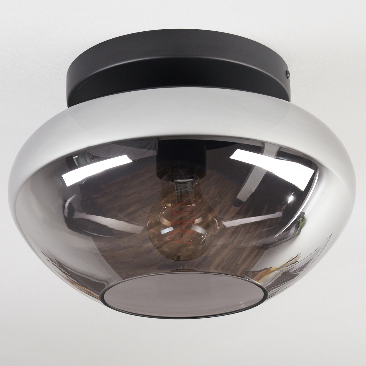 Eine moderne Deckenleuchte mit schwarzem Sockel und reflektierendem, rauchigem Glasschirm, der eine sichtbare Glühbirne enthält.
